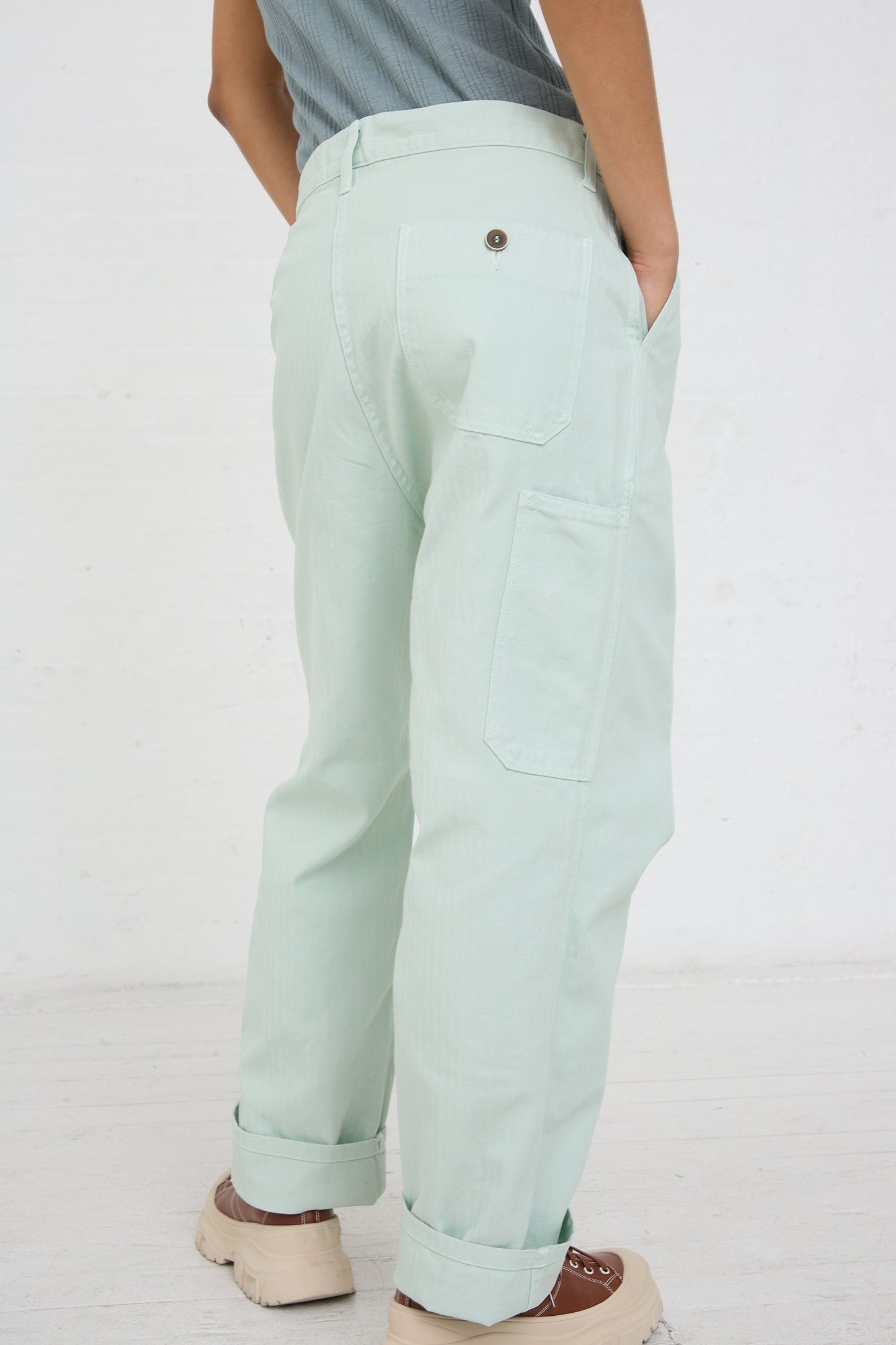 Person standing side-on, showcasing Ice Green Ichi Antiquités Herringbone Garment Dye Pant with back pocket details.