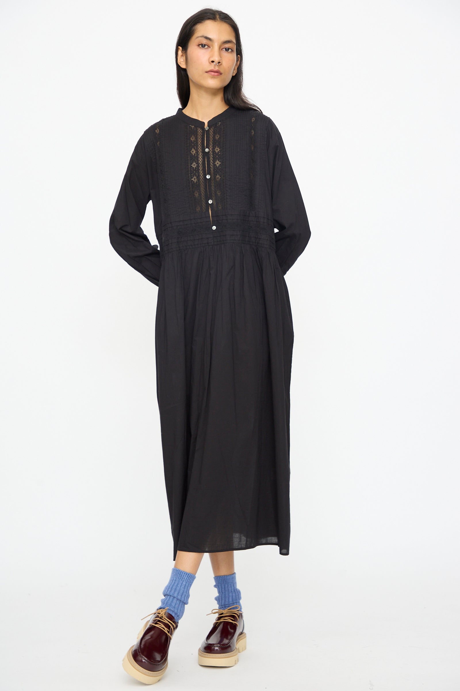 A woman stands against a white background wearing the Ichi Antiquités India Cotton Dress in Black, paired with blue socks and burgundy platform shoes.