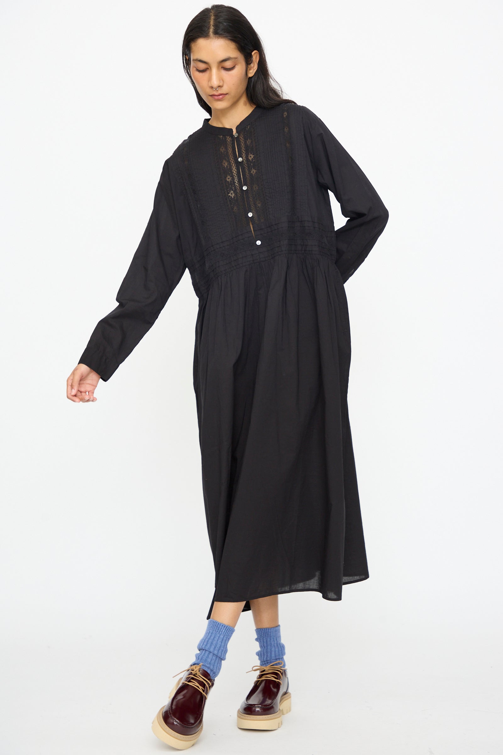 A person wearing the India Cotton Dress in Black by Ichi Antiquités, blue socks, and burgundy platform shoes stands against a plain white background.