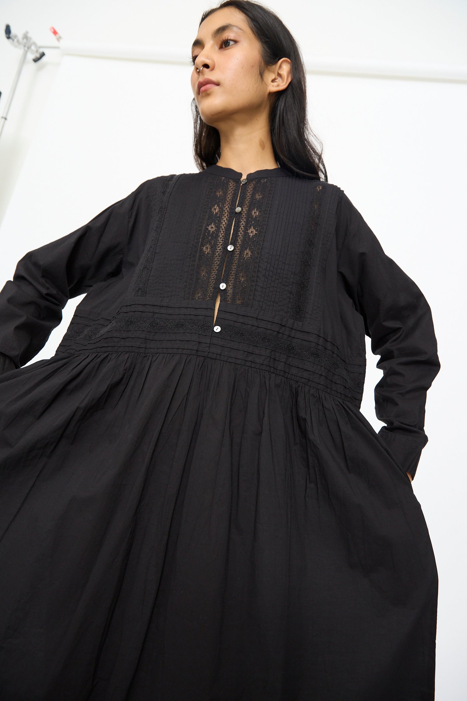A woman models the Ichi Antiquités India Cotton Dress in Black, featuring a loose fit with decorative embroidery and bodice buttons, set against a plain white background.