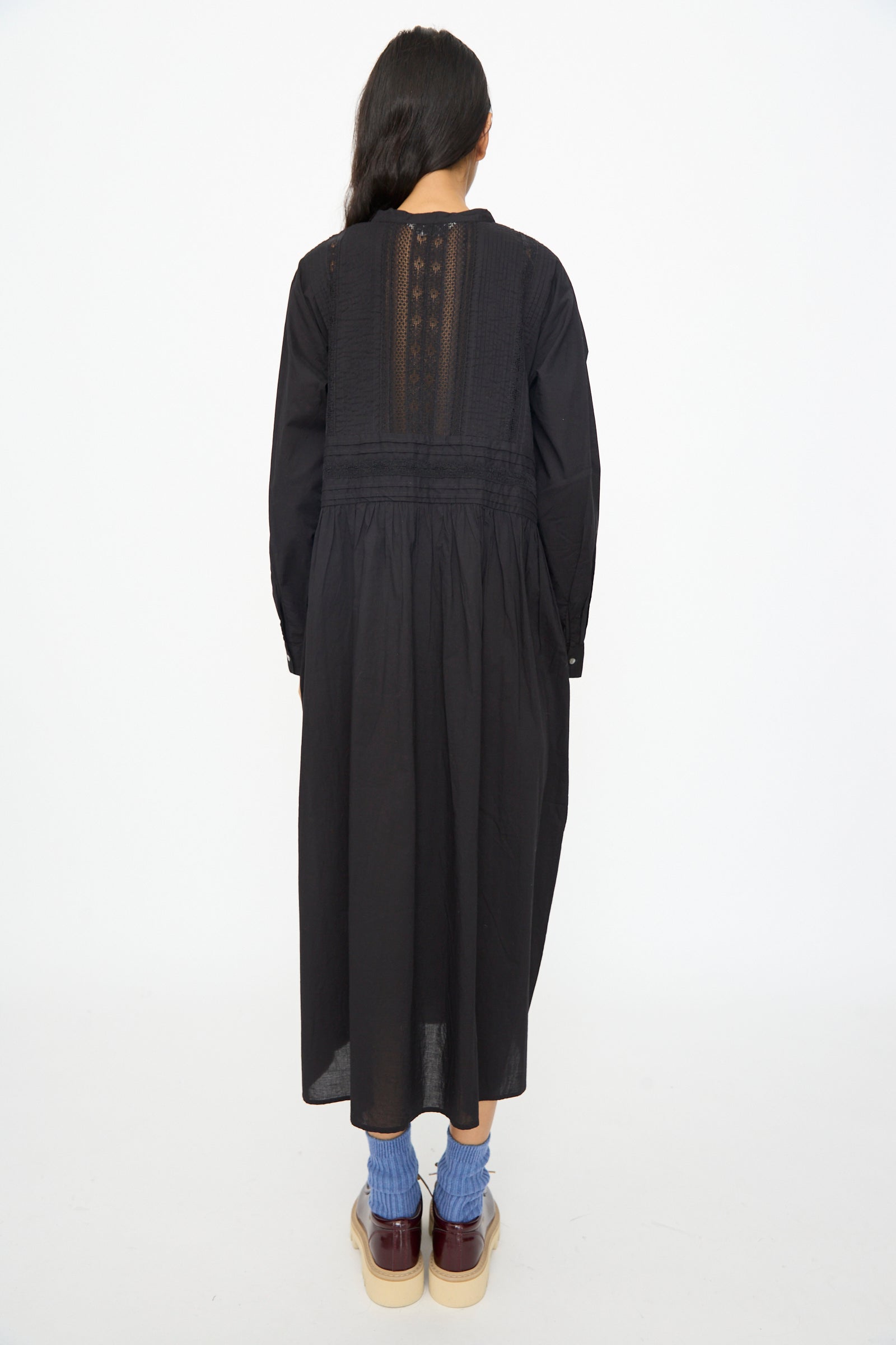 A person stands facing away, wearing the Ichi Antiquités India Cotton Dress in Black, styled with blue socks and platform shoes, against a plain white background.
