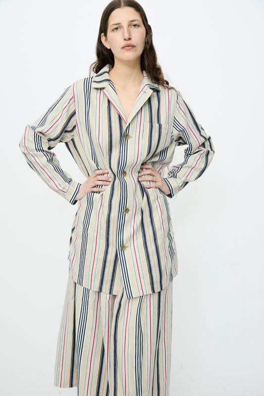 A person stands hands on hips, wearing the Ichi Antiquités Indigo Stripe Atelier Jacket in Multi, a long-sleeve oversized outfit with beige, navy, and red vertical stripes.