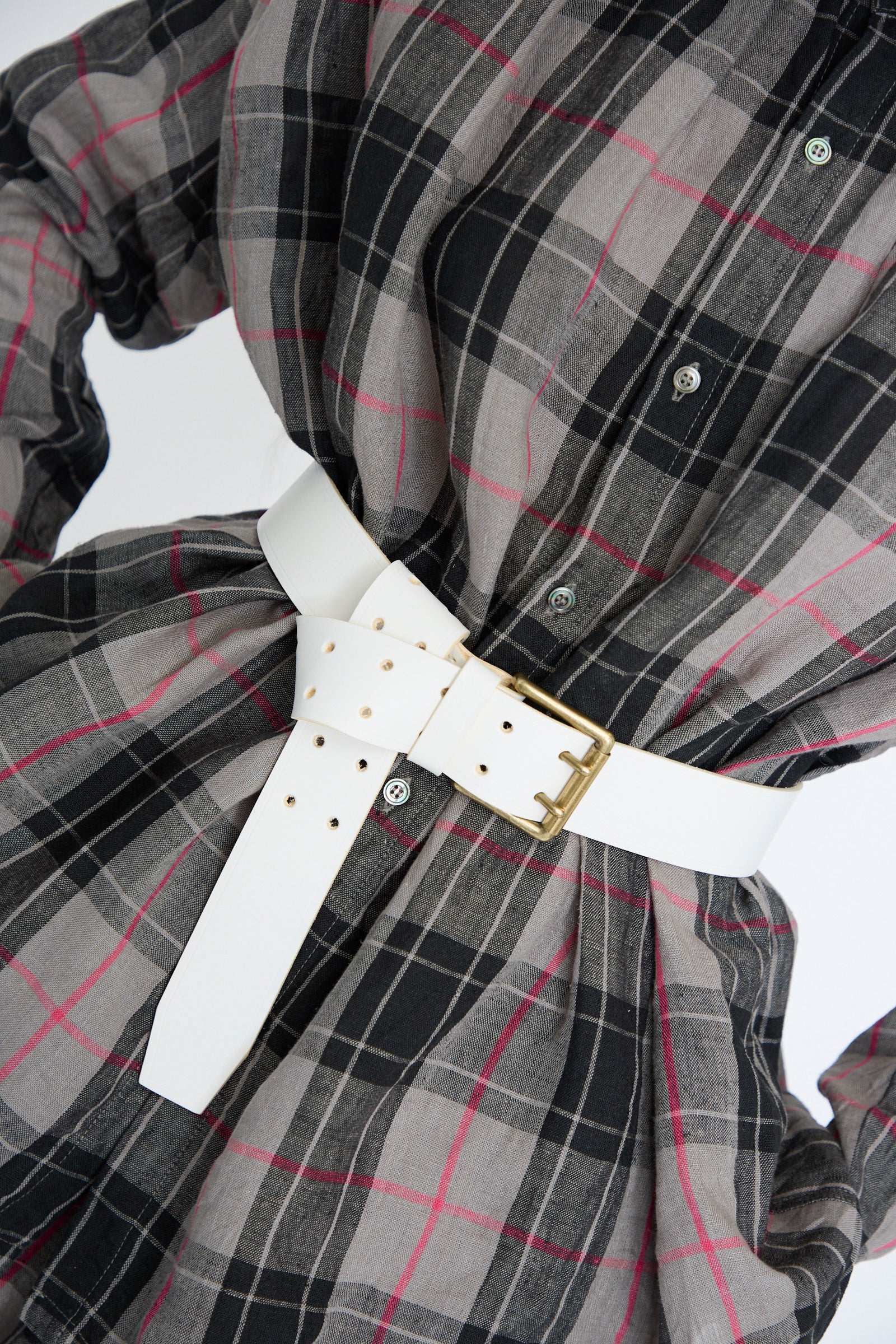 Close-up of a person wearing a black and gray plaid dress with pink stripes, cinched at the waist with an Ichi Antiquités leather belt in white featuring a prominent brass buckle.