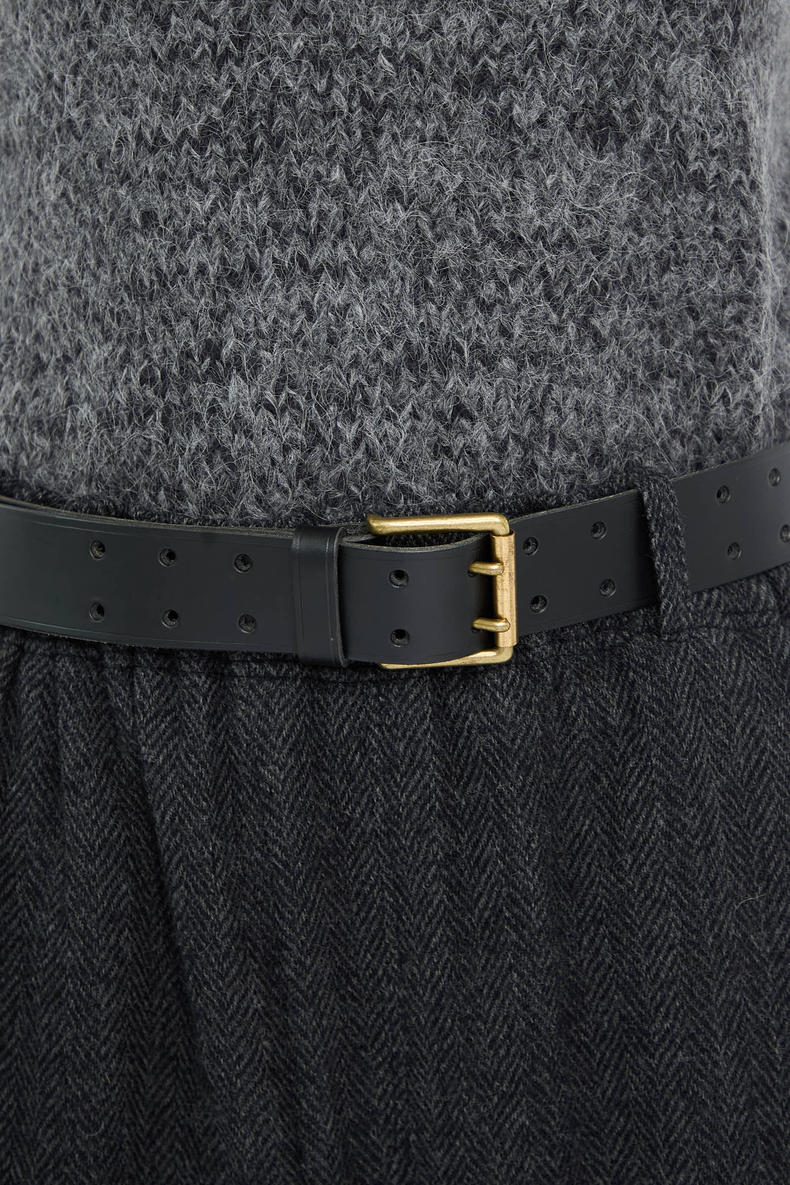 A sleek Leather Belt in black from Ichi Antiquités is styled over a grey knitted sweater and dark grey herringbone skirt.