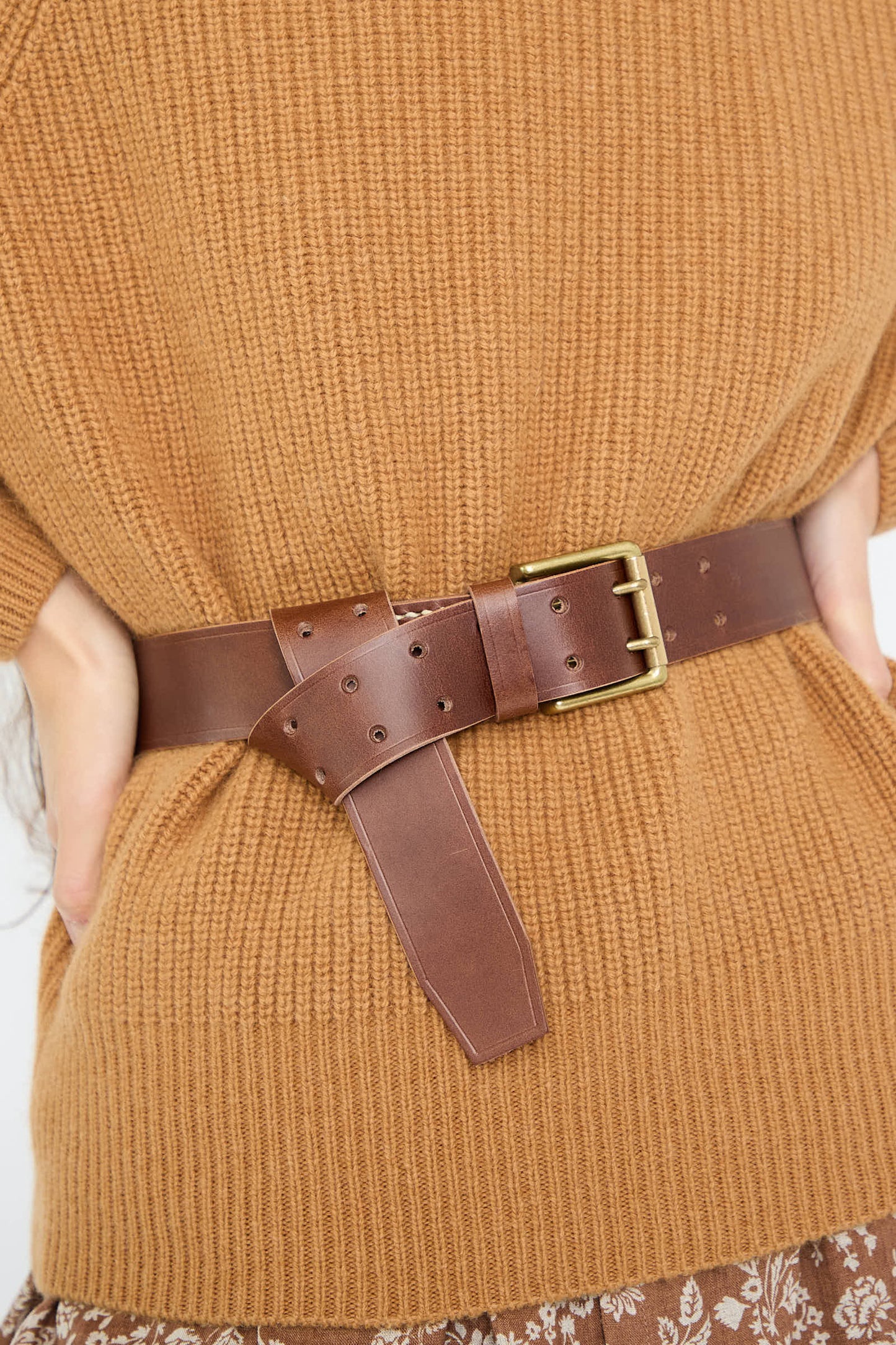 A person is wearing a Leather Belt in Dark Brown by Ichi Antiquités over a knitted sweater. The brass buckle secures it, with the tail hanging down.