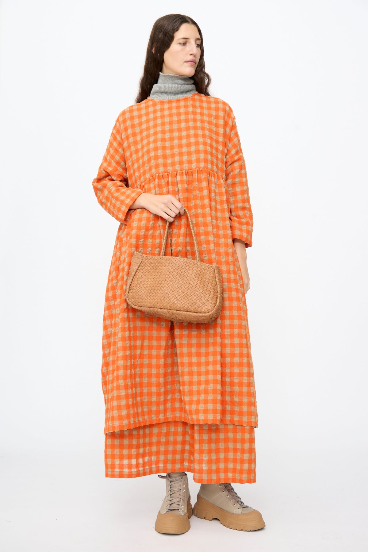 A person wearing an orange and beige checkered dress holds a small, brown Ichi Antiquités Leather Tote Bag in Brown.