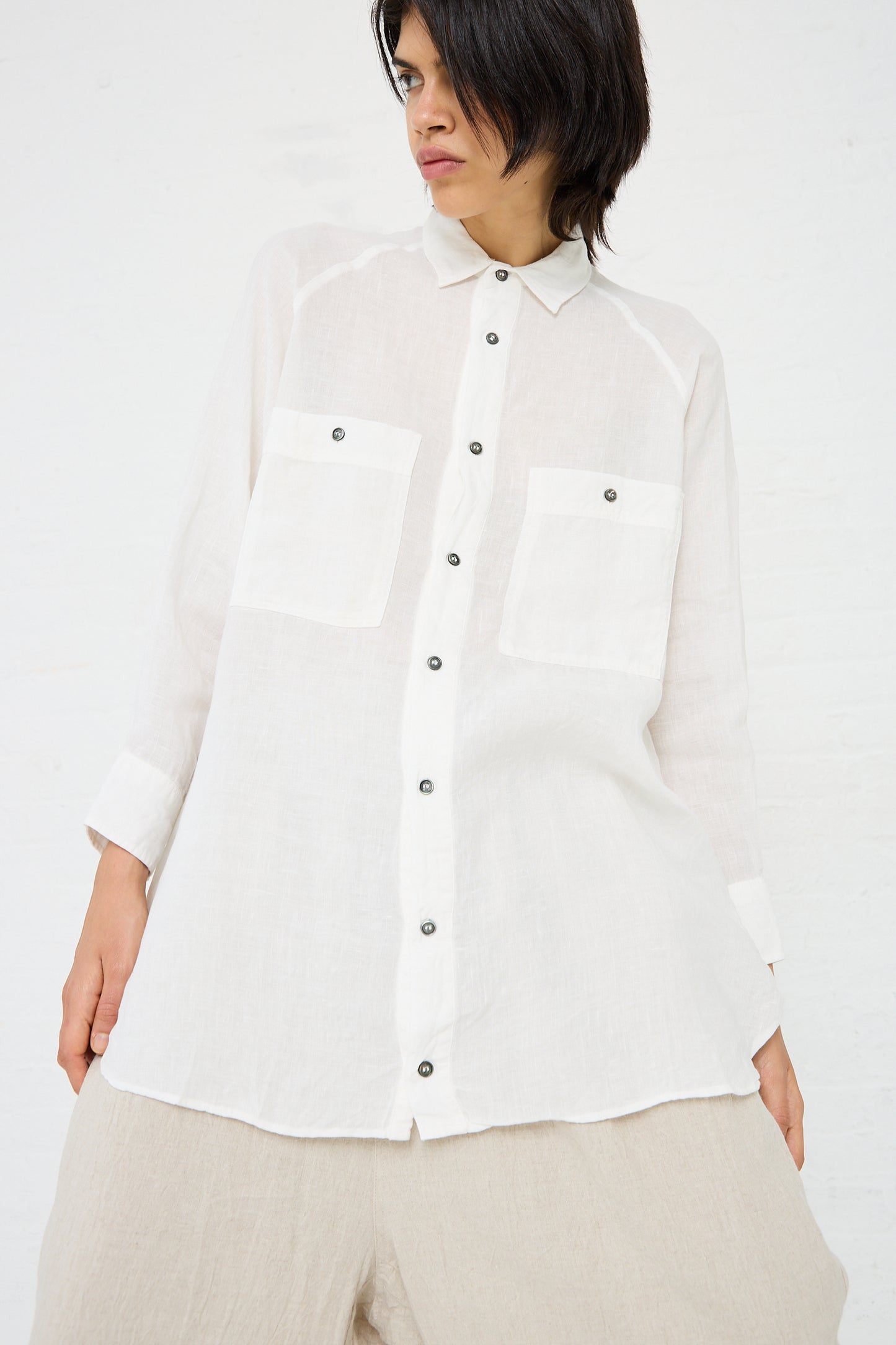 Person wearing an Ichi Antiquités Linen Canvas Overdye Shirt in White with two large front pockets, posing against a plain background. The oversized fit shirt is paired with beige pants.