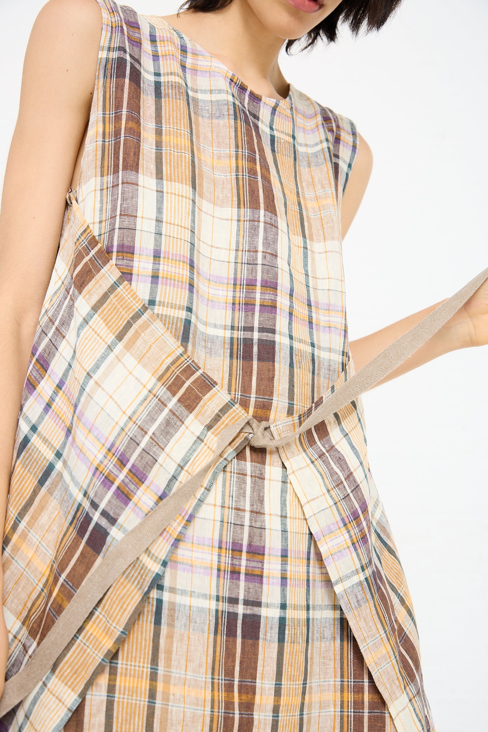 Close-up of a person wearing the Linen Check Dress in Beige by Ichi Antiquités, featuring a multicolor plaid pattern in brown, yellow, and white. The person is adjusting the wrap detail on the side of the dress.