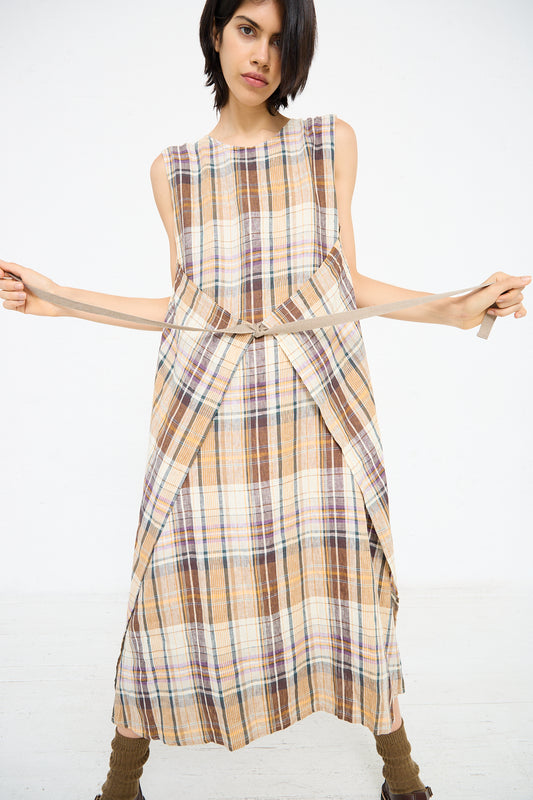 A person stands against a white background, wearing an Ichi Antiquités Linen Check Dress in Beige with wrap detail, holding both sides of a belt tied around the waist.