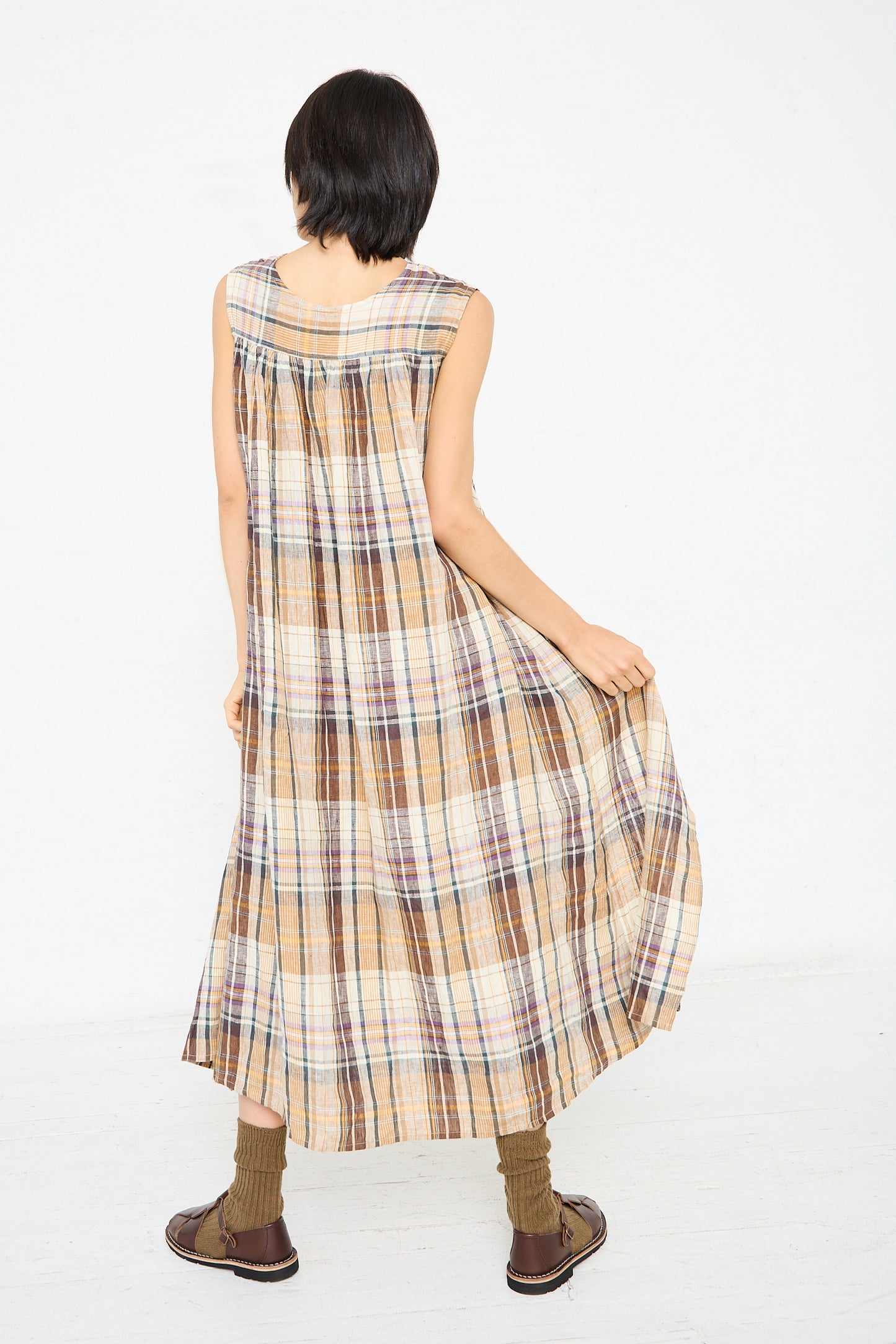 Person wearing a sleeveless, long Linen Check Dress in Beige by Ichi Antiquités and brown shoes stands with back to camera, holding out the sides of the dress.