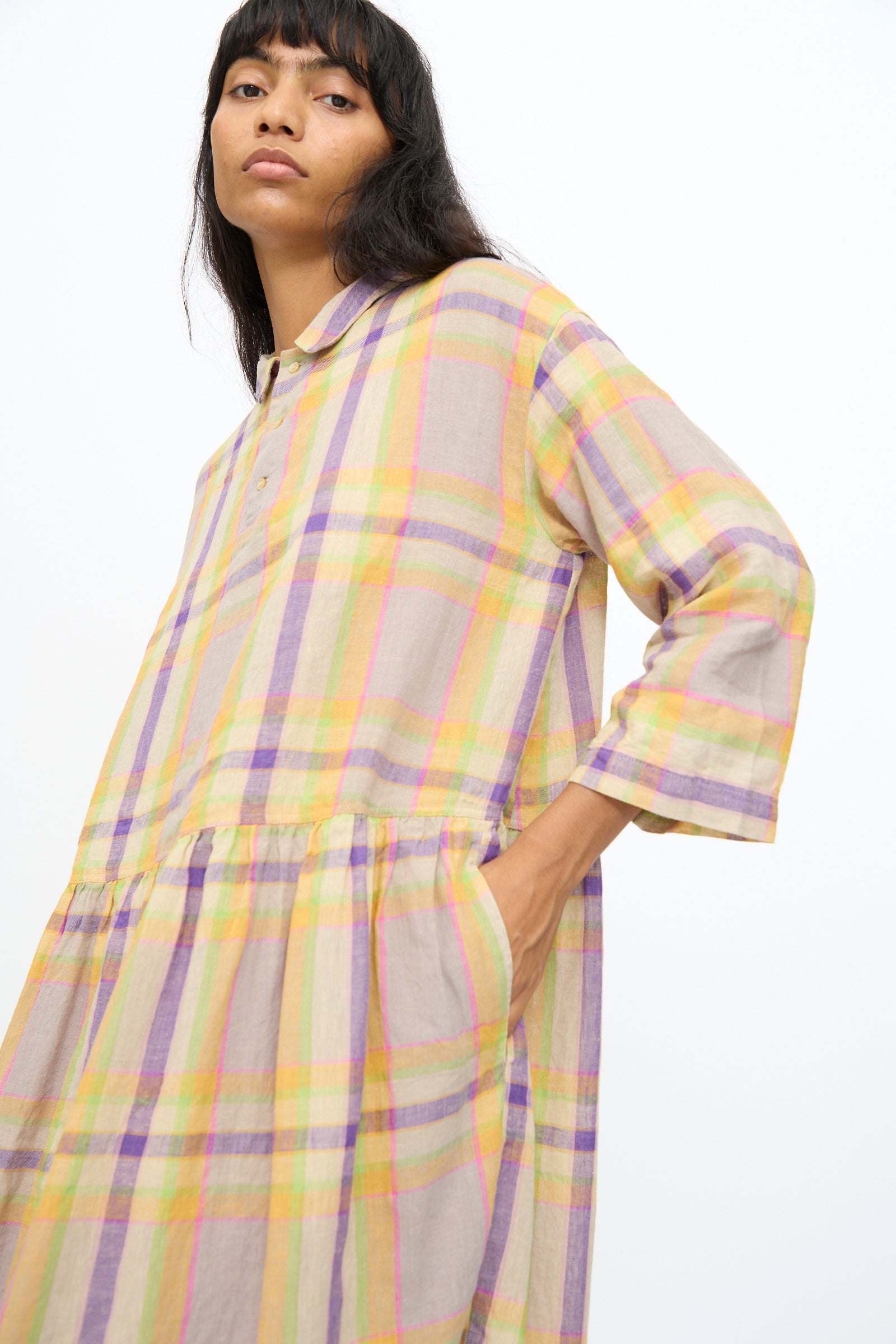 A person wears the Ichi Antiquités Linen Check Dress in Beige, featuring an oversized fit and a pastel plaid pattern of yellow, lavender, and pink, standing against a plain white background for a comfortable and chic look.