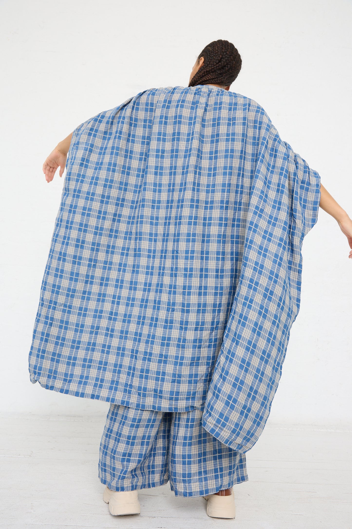 Person draped in a Linen Check Dress in Dark Indigo and Natural Linen from Ichi Antiquités standing against a white background.