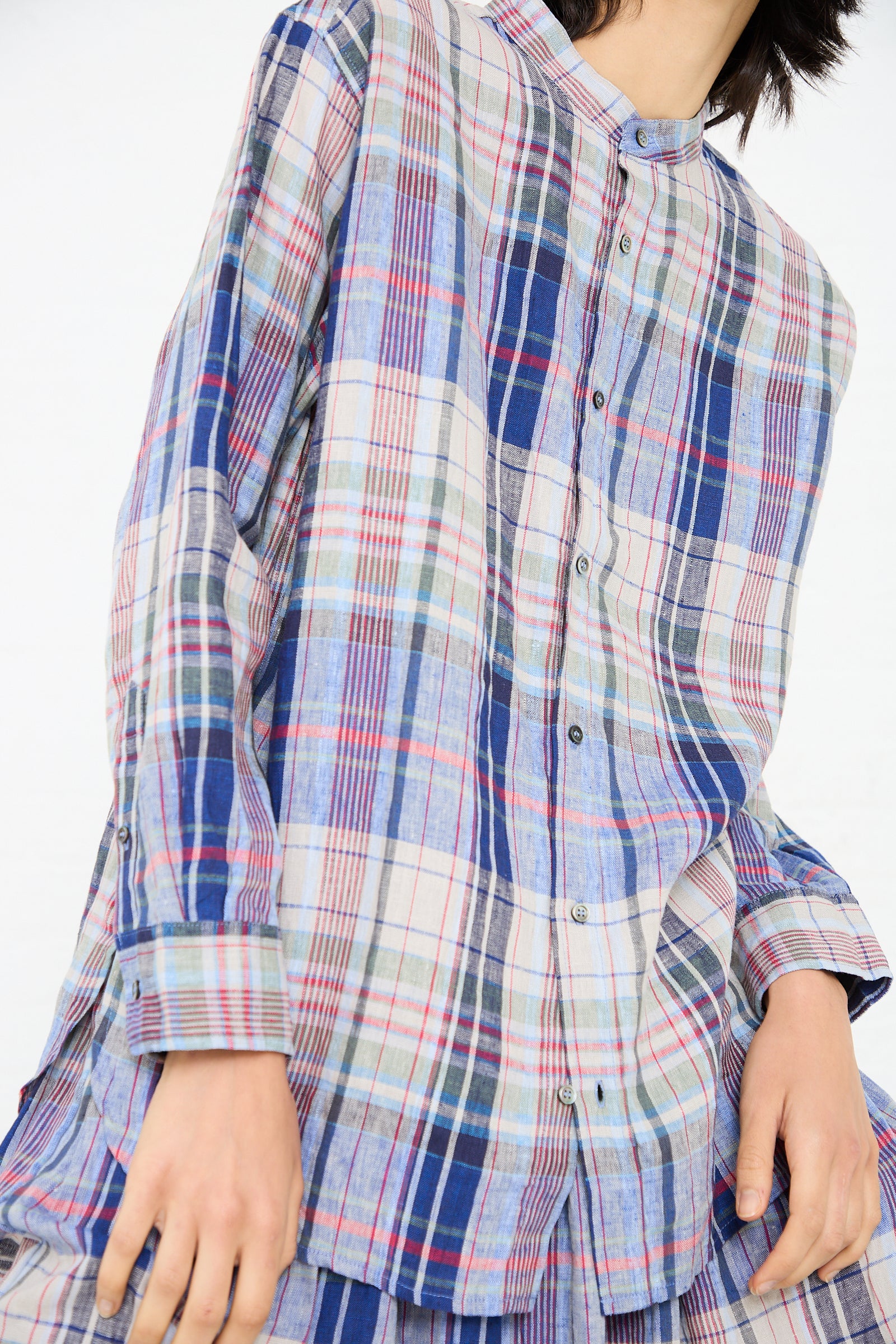 Person wearing an oversized, multicolored plaid linen shirt with long sleeves and buttoned front. The Linen Check Shirt in Navy by Ichi Antiquités, featuring shades of blue, red, green, and white, has a relaxed band collar that adds a touch of sophistication to its casual navy check pattern.