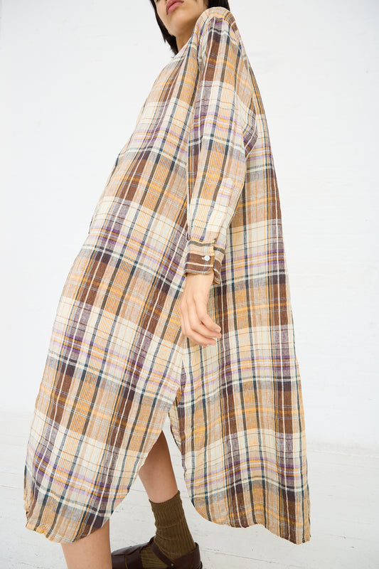 Person wearing a long, relaxed fit, multicolor Linen Check Shirt Dress in Beige by Ichi Antiquités with shades of brown, beige, and hints of purple, paired with brown socks and dark footwear, posing with one hand holding the dress.