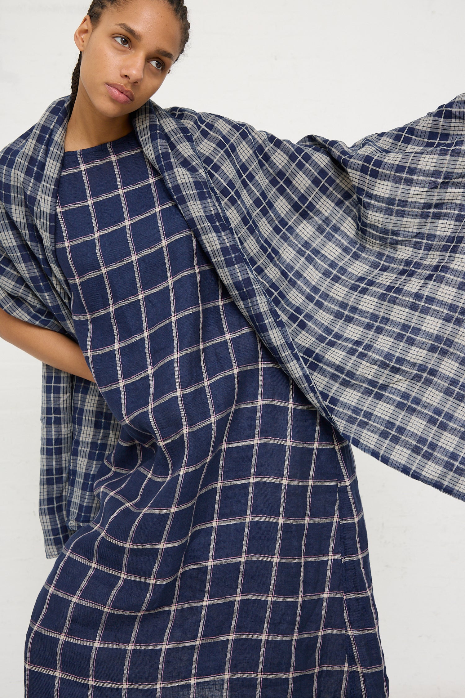 A woman posing in a blue plaid Ichi Antiquités dress with a flowing sleeve design, complemented by an Ichi Antiquités Linen Check Stole in Dark Indigo and Natural.