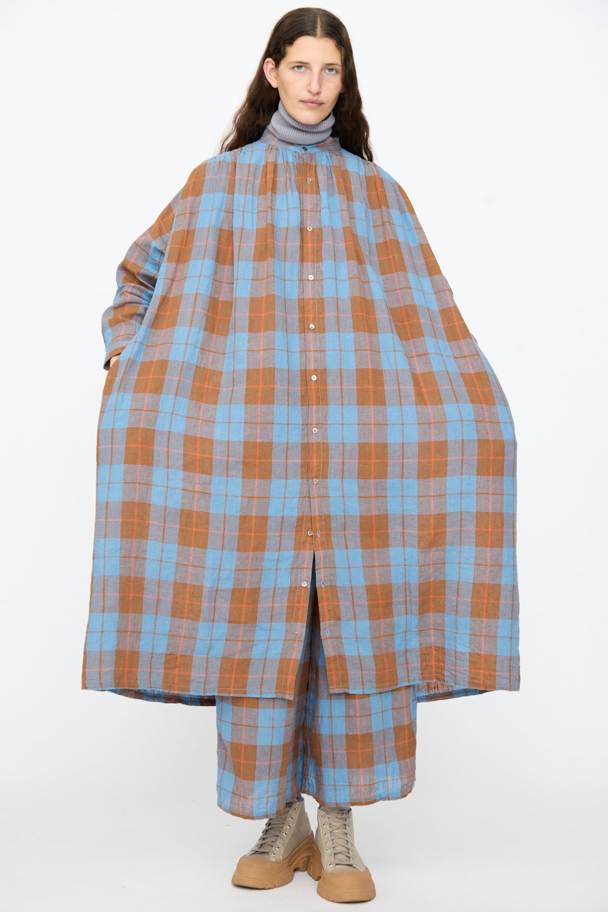 A person wearing an oversized Ichi Antiquités Linen Cotton Check Dress in Blue over a grey turtleneck with matching plaid wide-leg trousers and beige sneakers.
