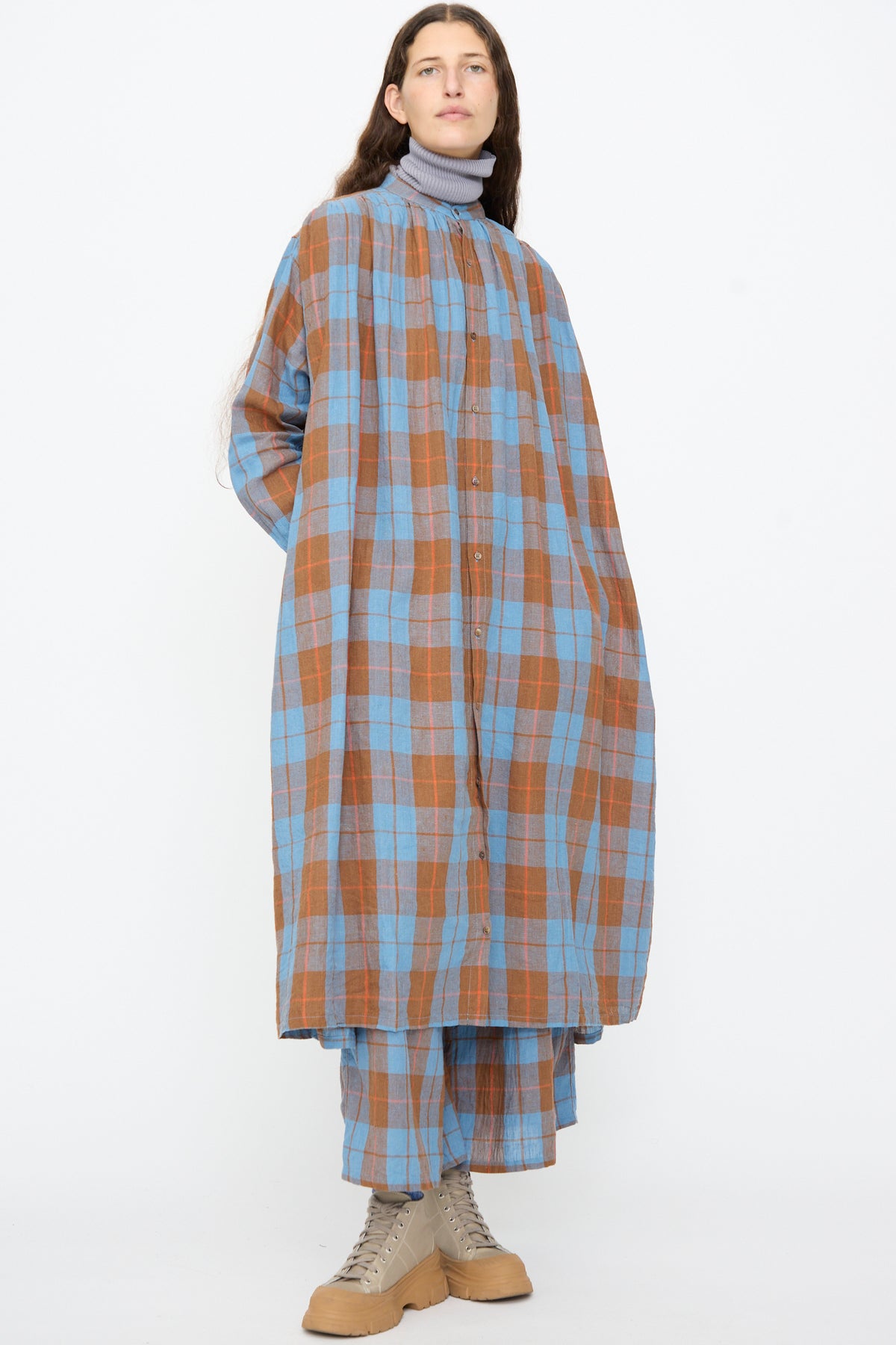 A person wearing an Ichi Antiquités Linen Cotton Check Dress in Blue with matching trousers over a gray mock-neck top and beige boots.