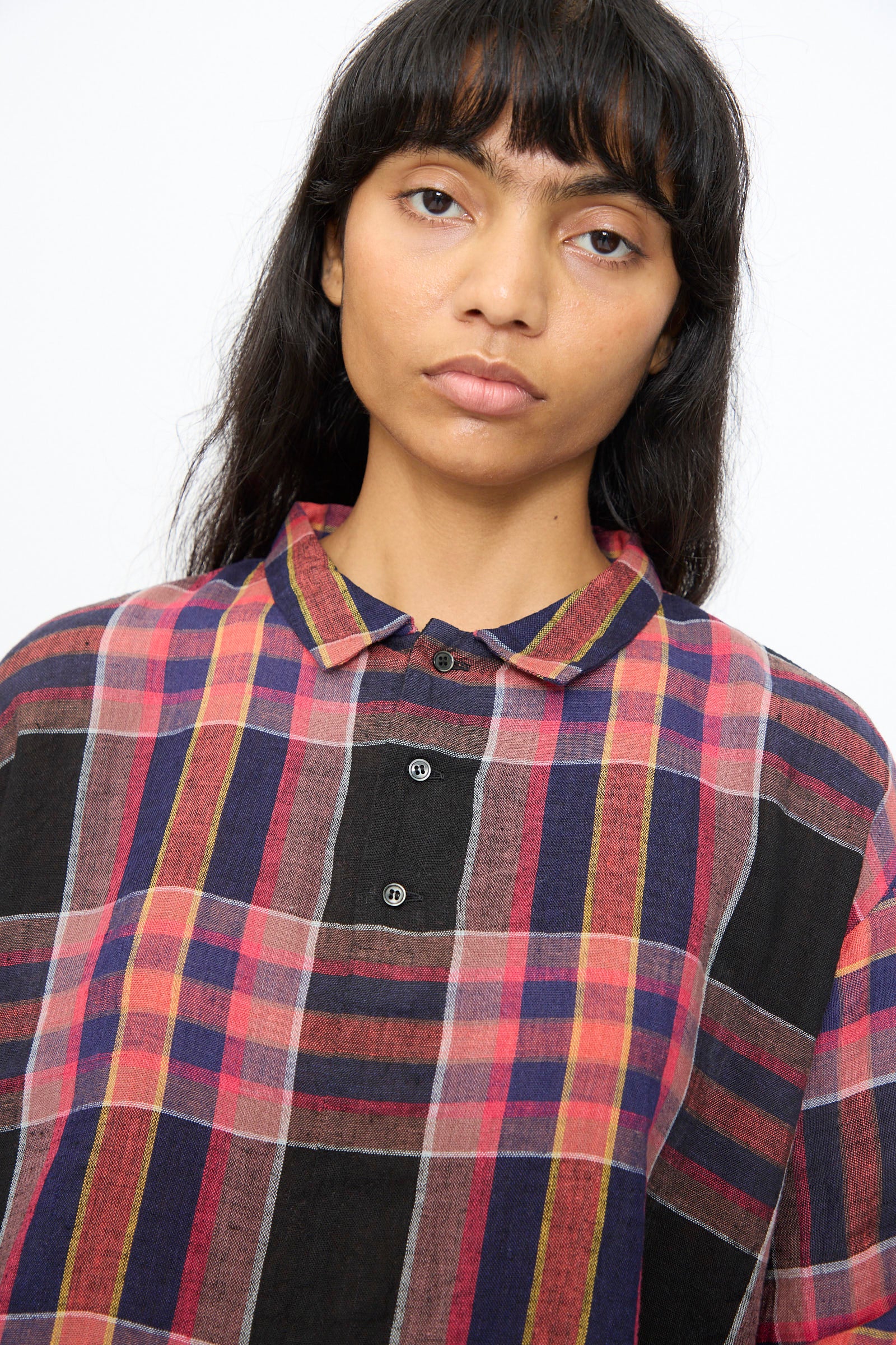 A person with long dark hair and bangs wears the Ichi Antiquités Linen Cotton Check Shirt in Black, featuring a colorful plaid pattern, made in Japan, posed against a plain white background.