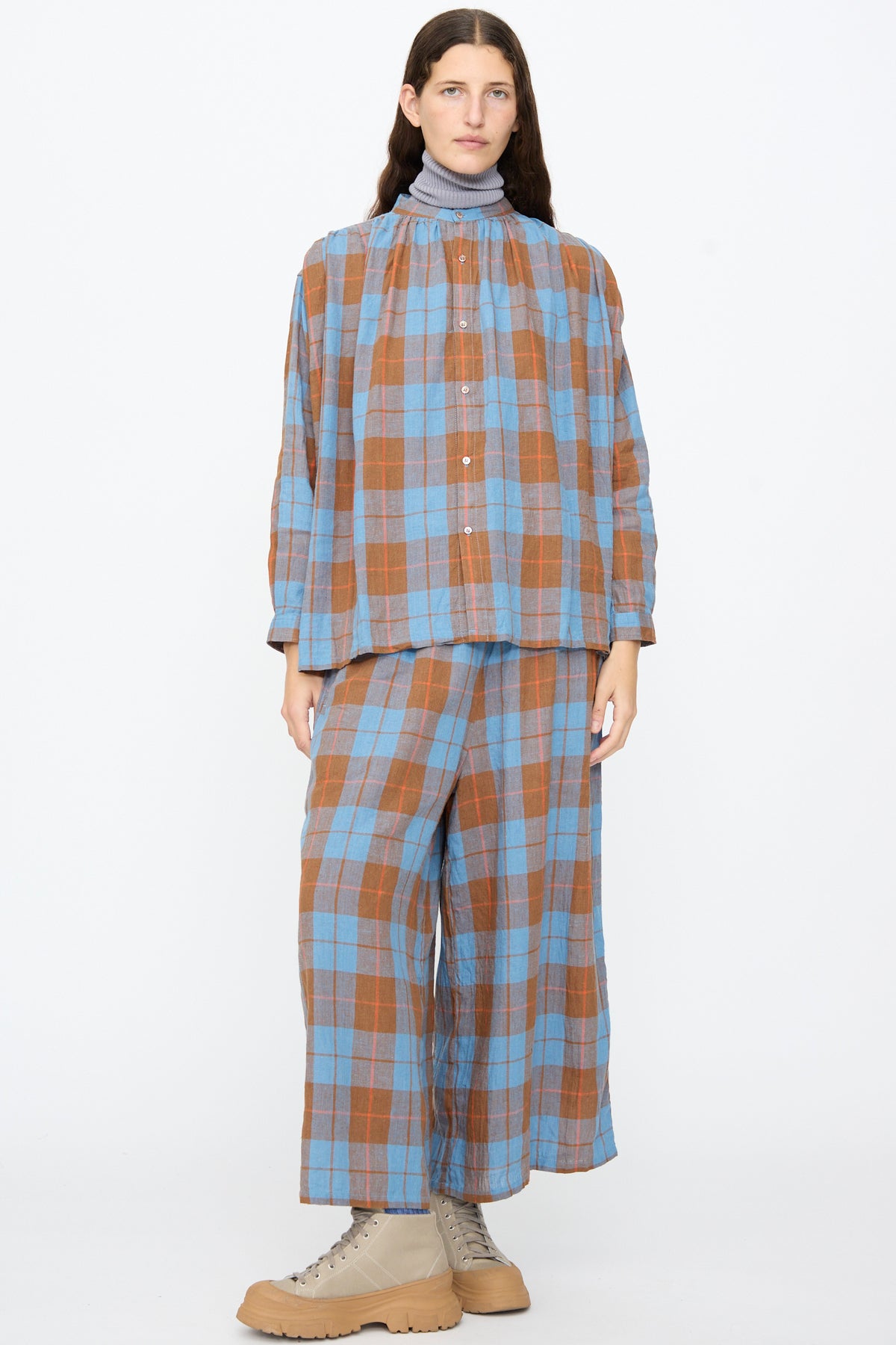 A person wears an Ichi Antiquités Linen Cotton Check Shirt in Blue and matching wide-leg pants over a grey mock-neck top, paired with tan lace-up boots.