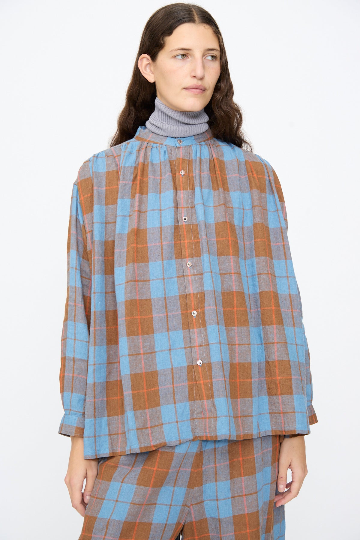 Ichi Antiquités Linen Cotton Check Shirt in Blue, featuring a long-sleeved, blue and brown gingham pattern with a band collar, worn over a grey turtleneck.