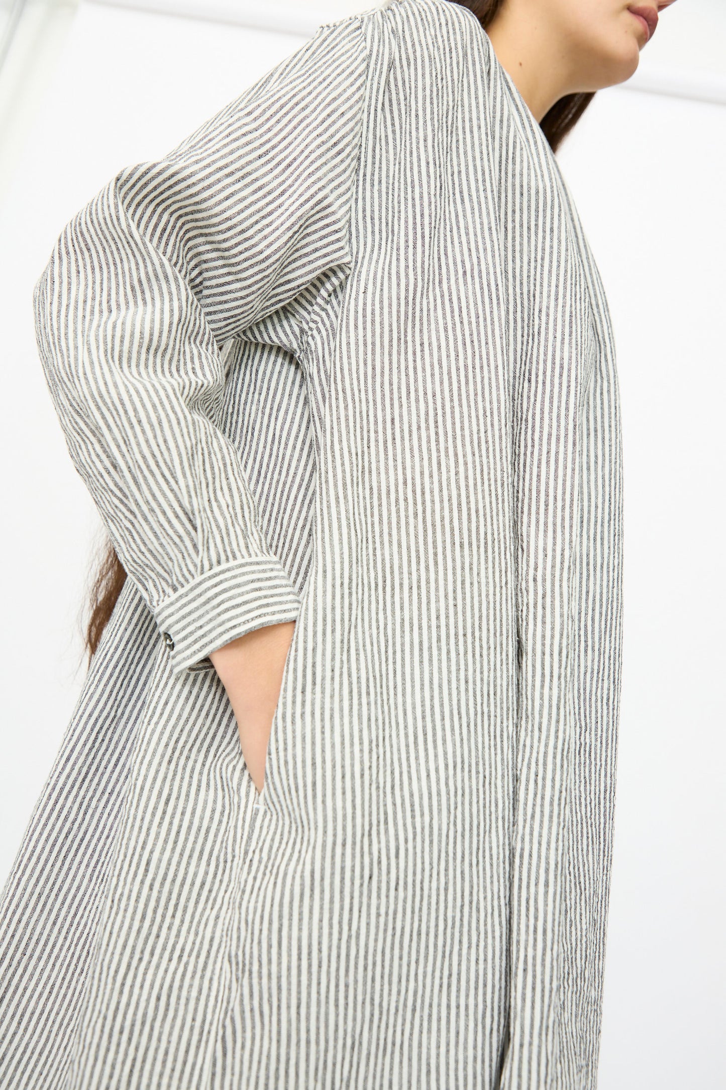 A person wearing the Ichi Antiquités Linen and Cotton Dress in White Stripe, with one hand in a side pocket, is photographed from a low angle.
