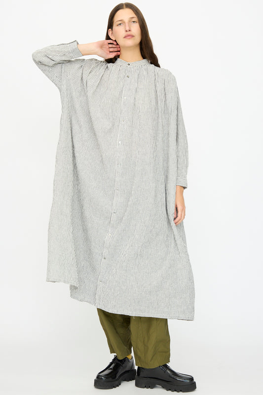 A person wears the Ichi Antiquités Linen and Cotton Dress in White Stripe over olive green pants and black platform shoes, standing against a plain light background.