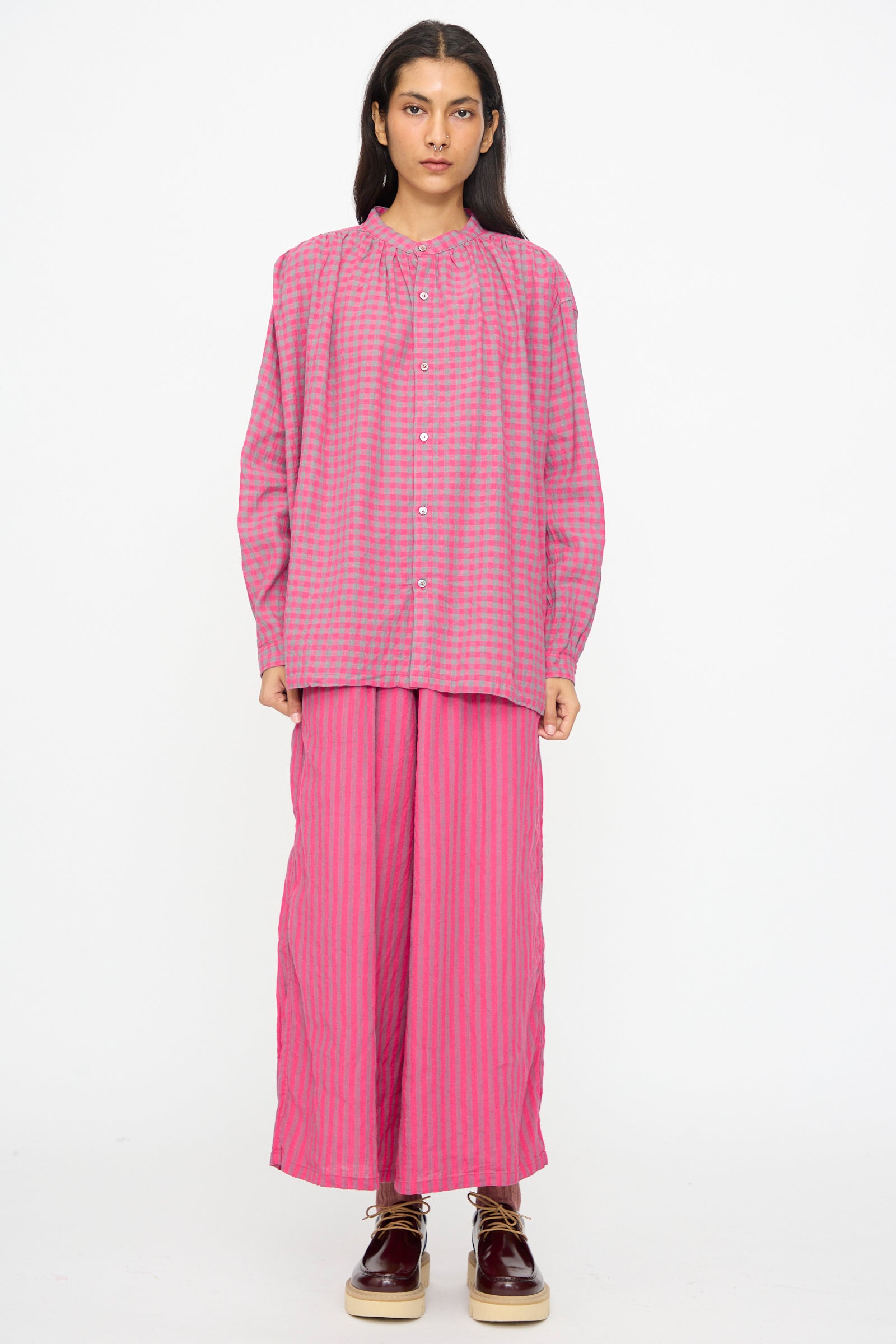 A person stands facing forward against a plain white background, wearing the Ichi Antiquités Linen Cotton Gingham Check Shirt in Pink, styled loosely with matching wide-leg pants and brown shoes.