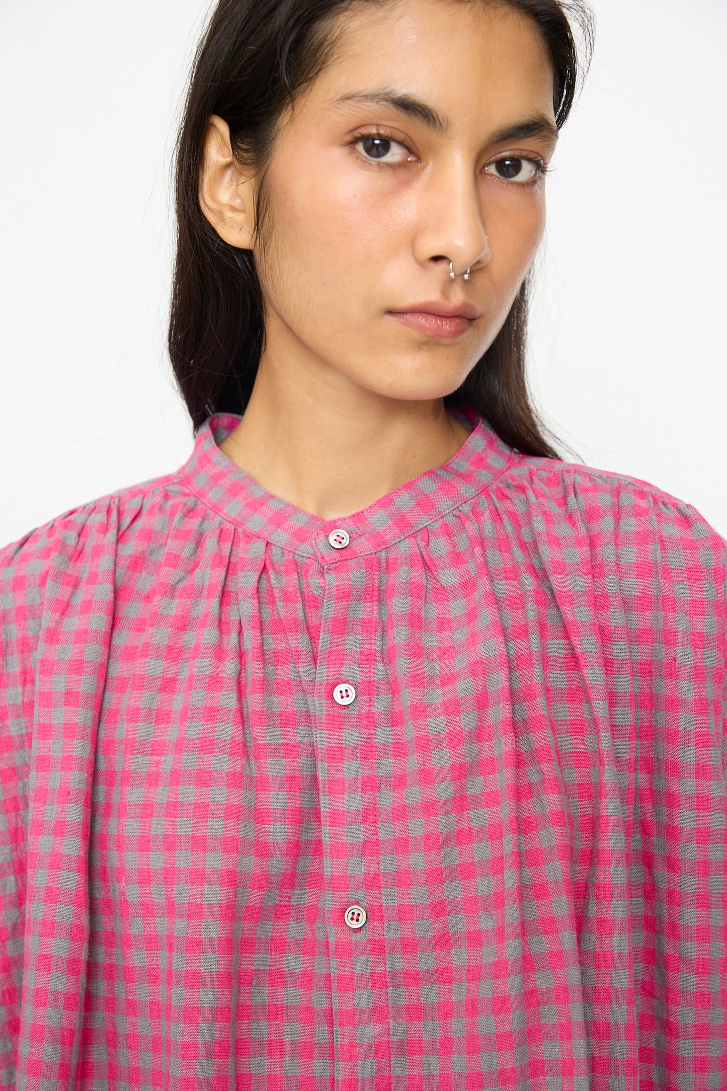 A person with long dark hair, wearing the Ichi Antiquités Linen Cotton Gingham Check Shirt in Pink and a silver nose ring, looks at the camera with a neutral expression.