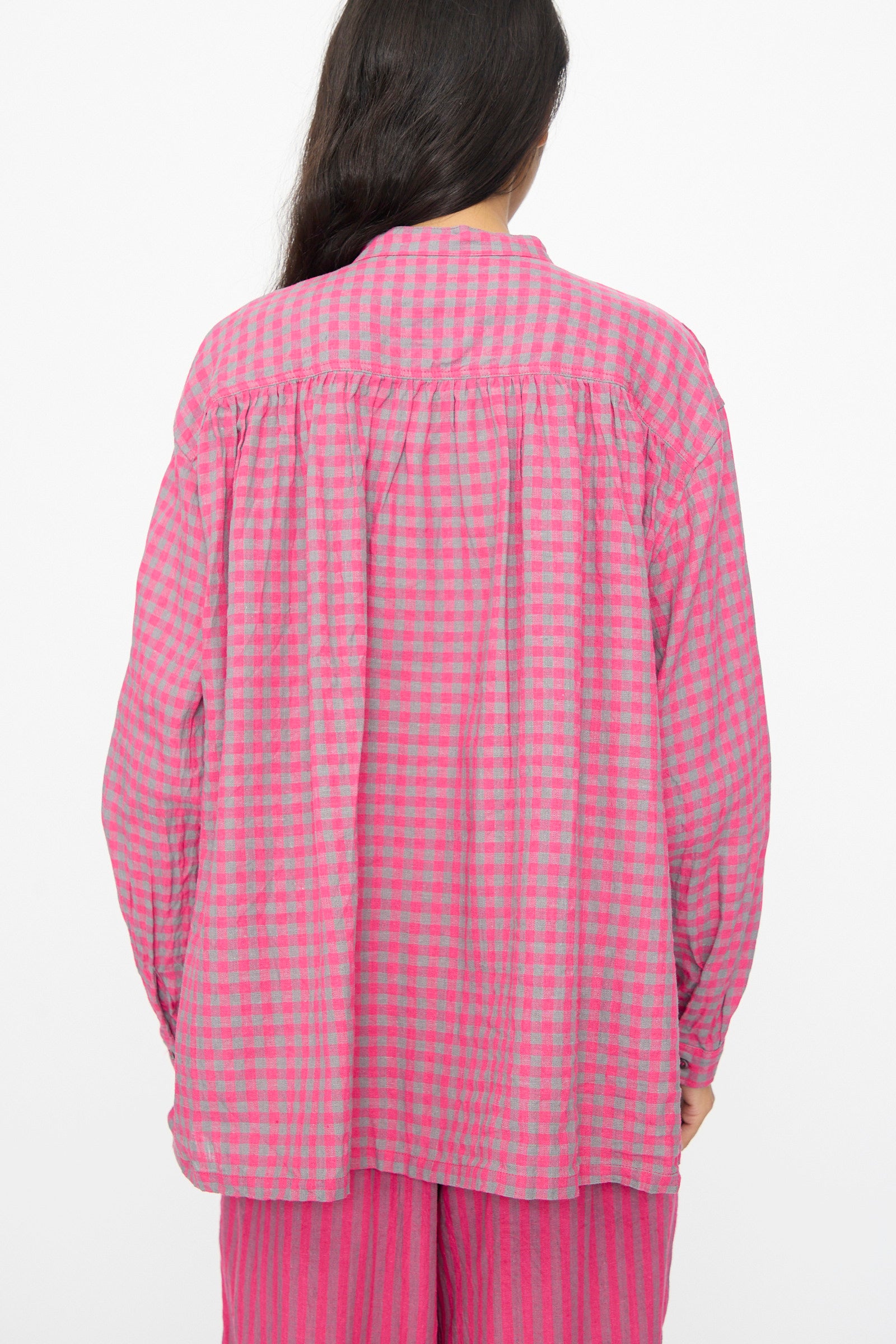 A person with long dark hair is seen from the back, wearing the Ichi Antiquités Linen Cotton Gingham Check Shirt in Pink—a loose-fitting, band-collared top crafted in a comfy linen cotton blend.