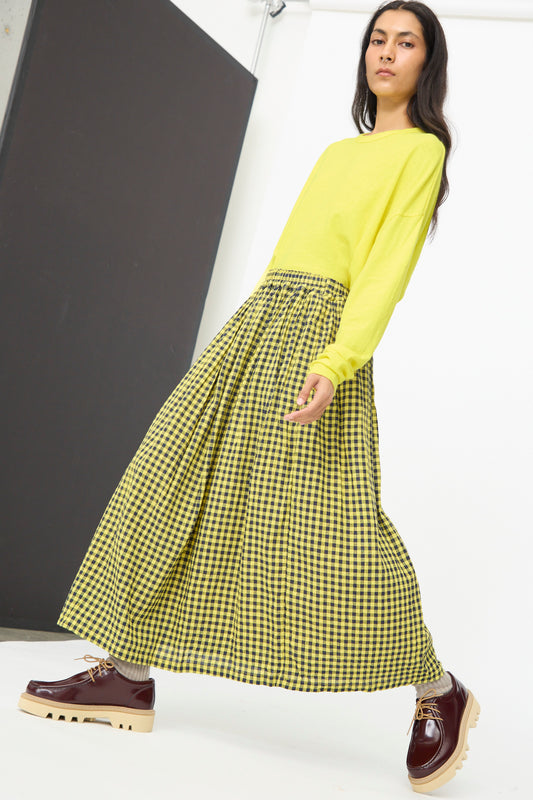 A person walks indoors wearing a yellow long-sleeve shirt, the Ichi Antiquités Linen Cotton Gingham Check Skirt in Yellow, and burgundy platform shoes.