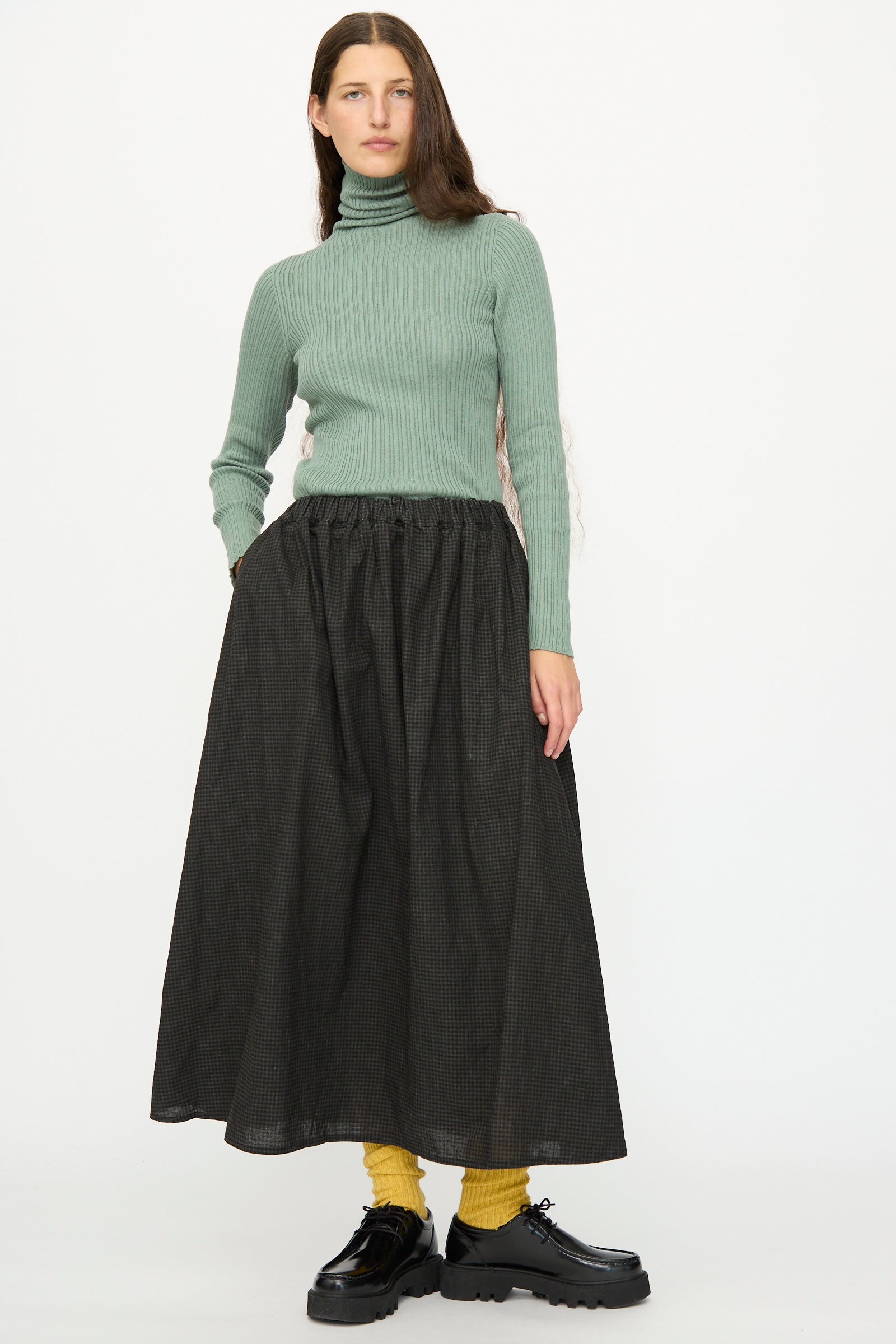 A person wearing a light green ribbed turtleneck, yellow socks, black platform shoes, and the Ichi Antiquités Linen Cotton Gingham Sumi Skirt in Check stands against a plain white background.