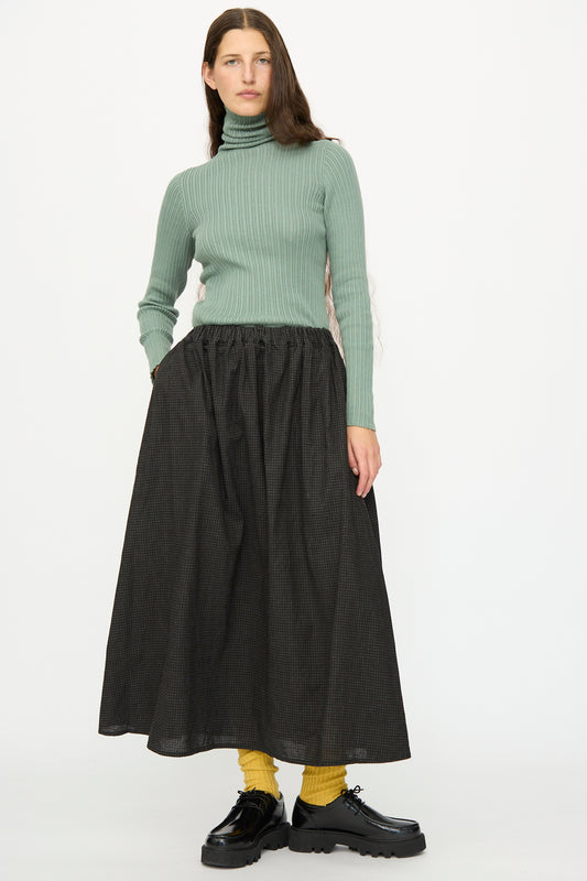 A person wearing a light green ribbed turtleneck, yellow socks, black platform shoes, and the Ichi Antiquités Linen Cotton Gingham Sumi Skirt in Check stands against a plain white background.