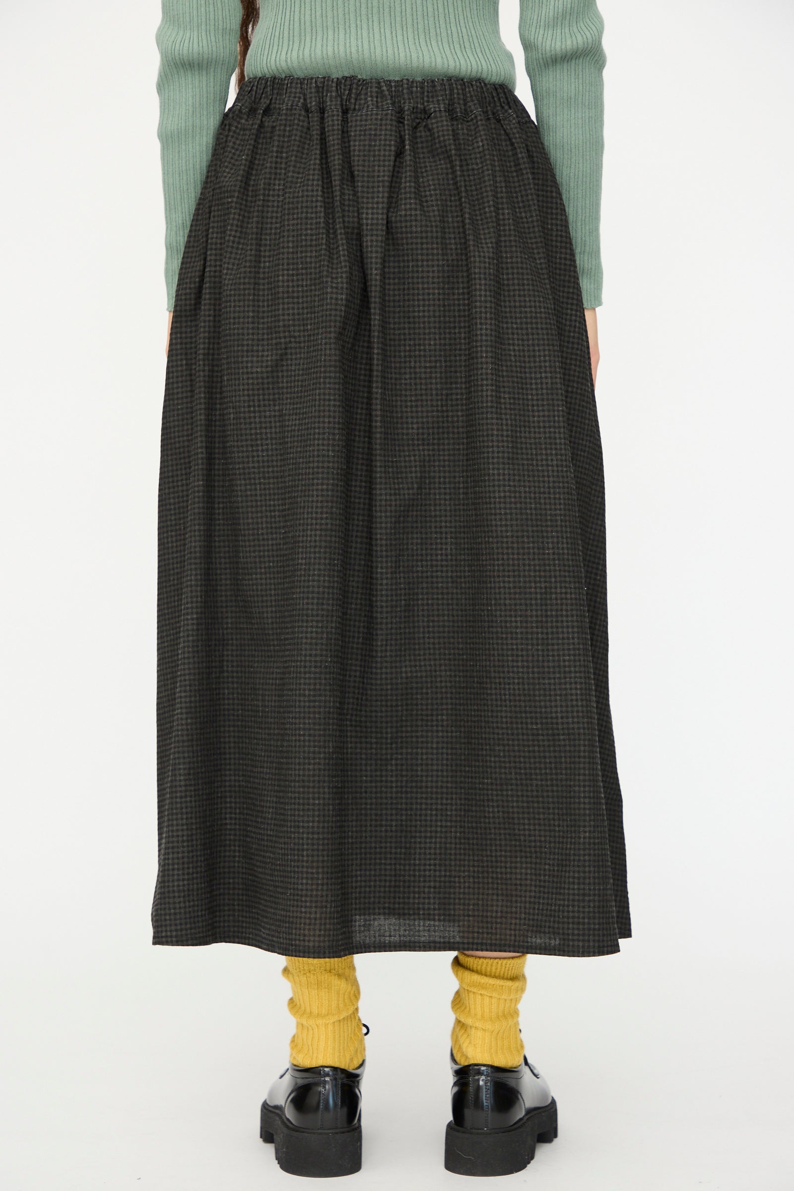 Someone stands against a plain white background wearing a green sweater, yellow socks, black shoes, and the Ichi Antiquités Linen Cotton Gingham Sumi Skirt in Check.
