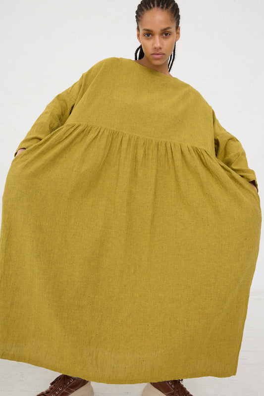 A woman in an oversized yellow Linen Cotton Herringbone Dress by Ichi Antiquités with a gathered waistline standing against a white background.