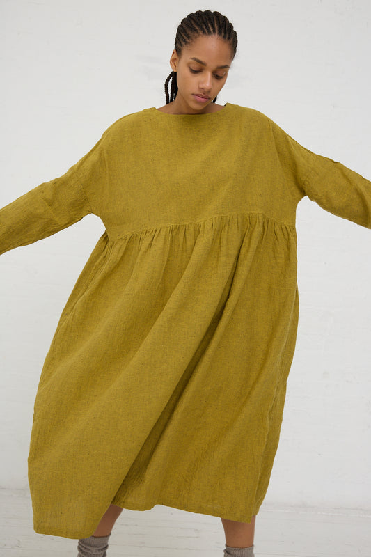 A person in a voluminous yellow Linen Cotton Herringbone dress with long sleeves, standing against a white background by Ichi Antiquités.
