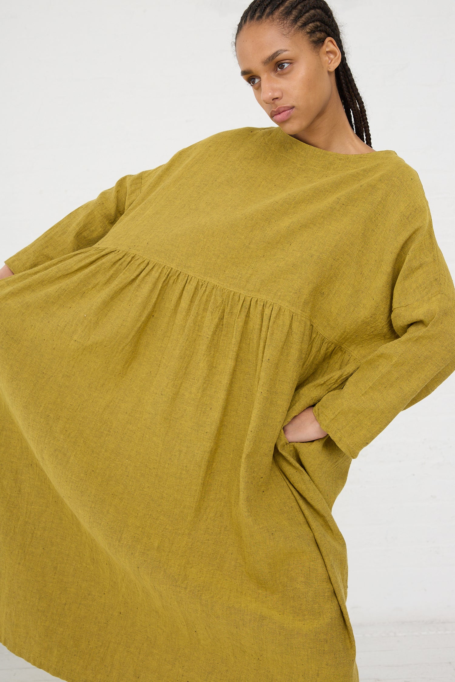 A woman in a loose-fitting, Linen Cotton Herringbone Dress in Yellow from Ichi Antiquités with her hand on her hip, against a white background.