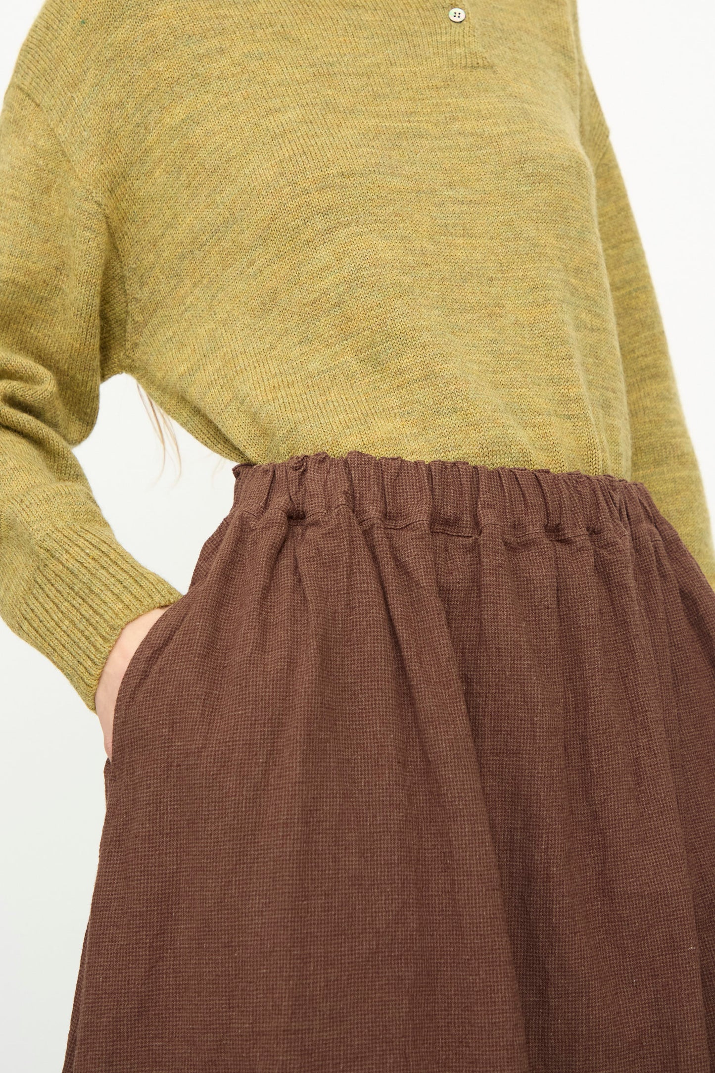 A person wears the Ichi Antiquités Linen Cotton Houndstooth Skirt in Brown, paired with a mustard yellow knit sweater, tucked in and hands in the skirt’s pockets.