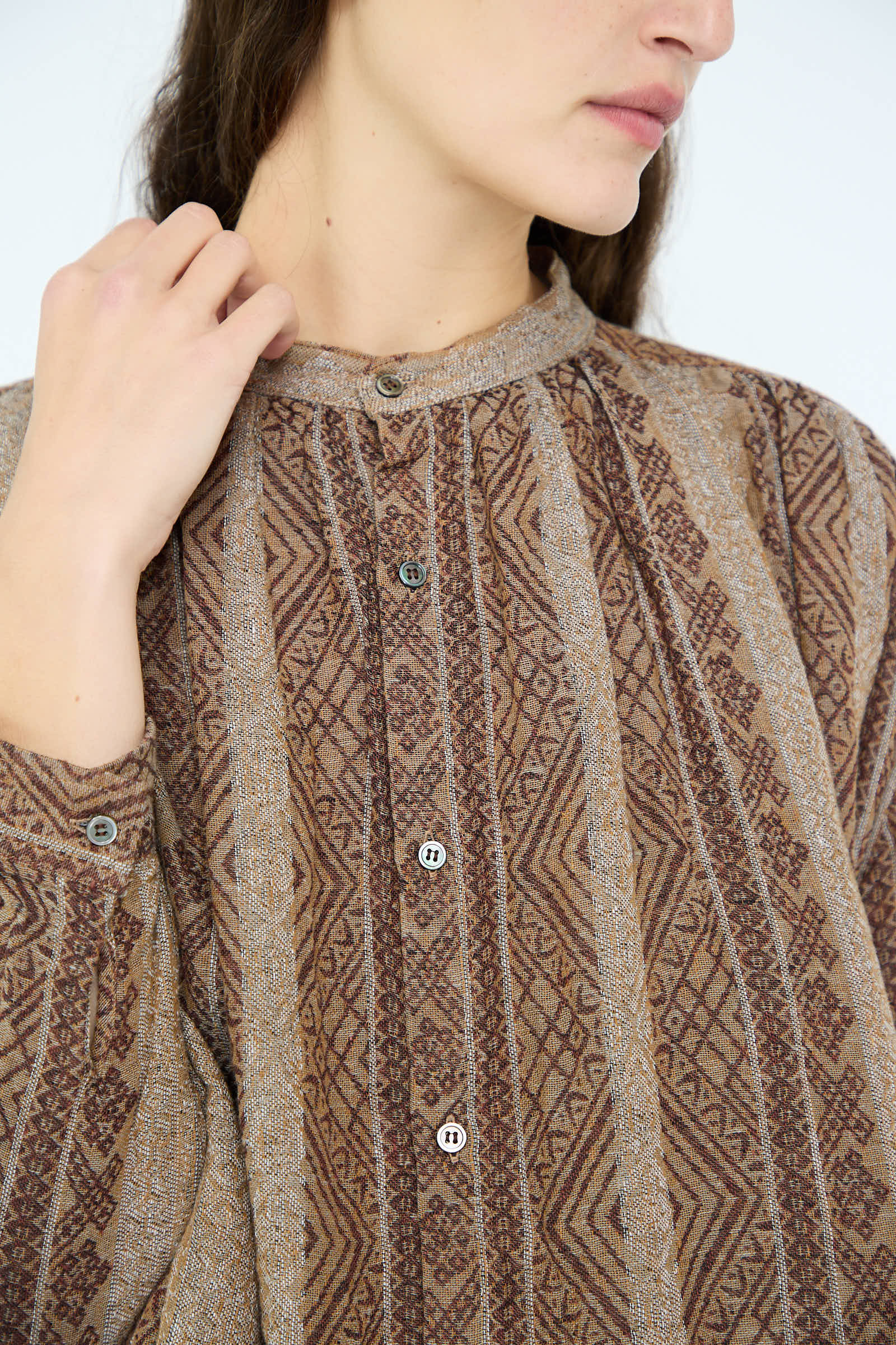 An individual is seen thoughtfully adjusting the band collar of an oversized Linen Cotton Jacquard Shirt in Brown by Ichi Antiquités.