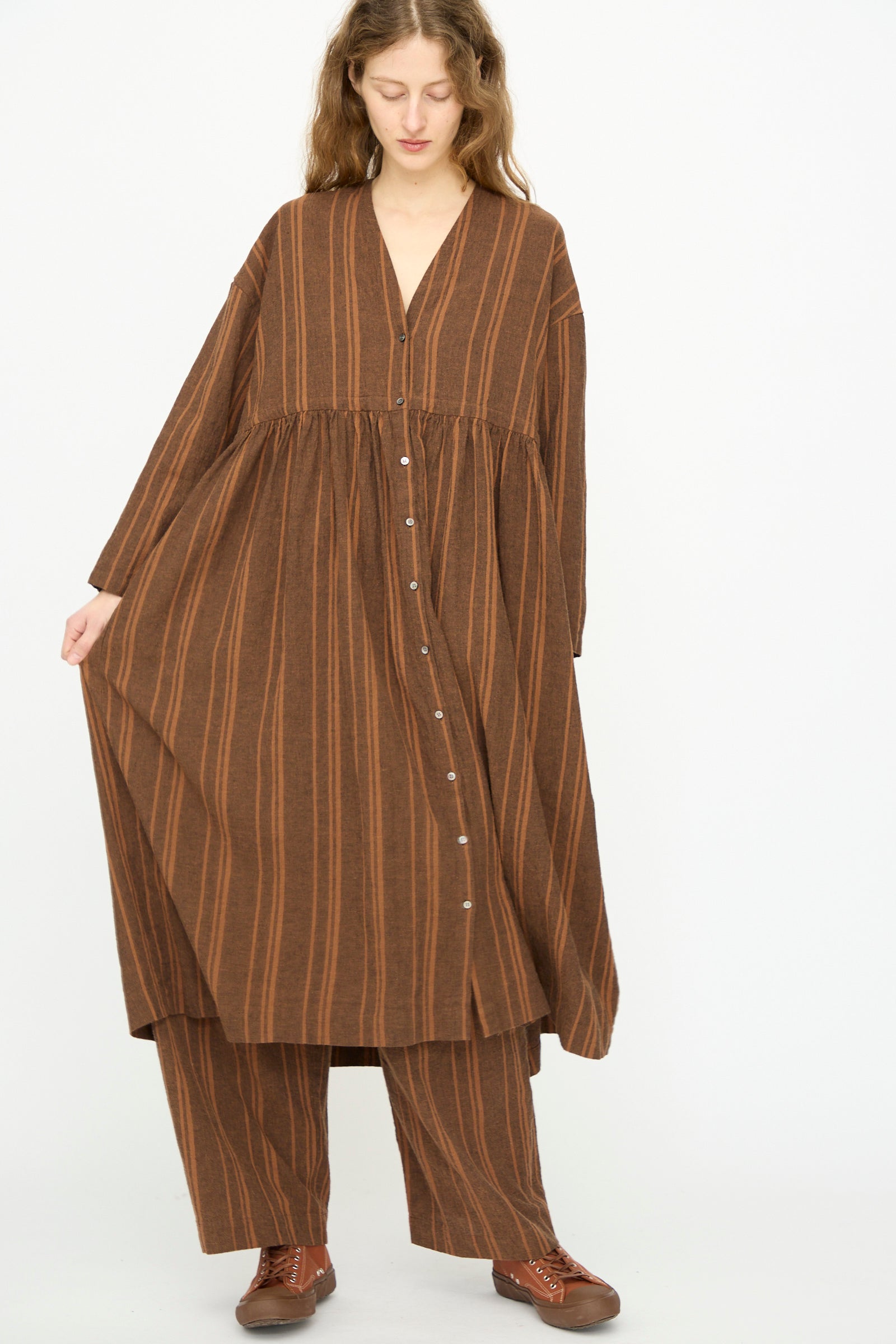 A person wears the Ichi Antiquités Linen Cotton Random Stripe Dress in Brown, styled with matching wide-leg pants and brown shoes, standing against a plain white background.