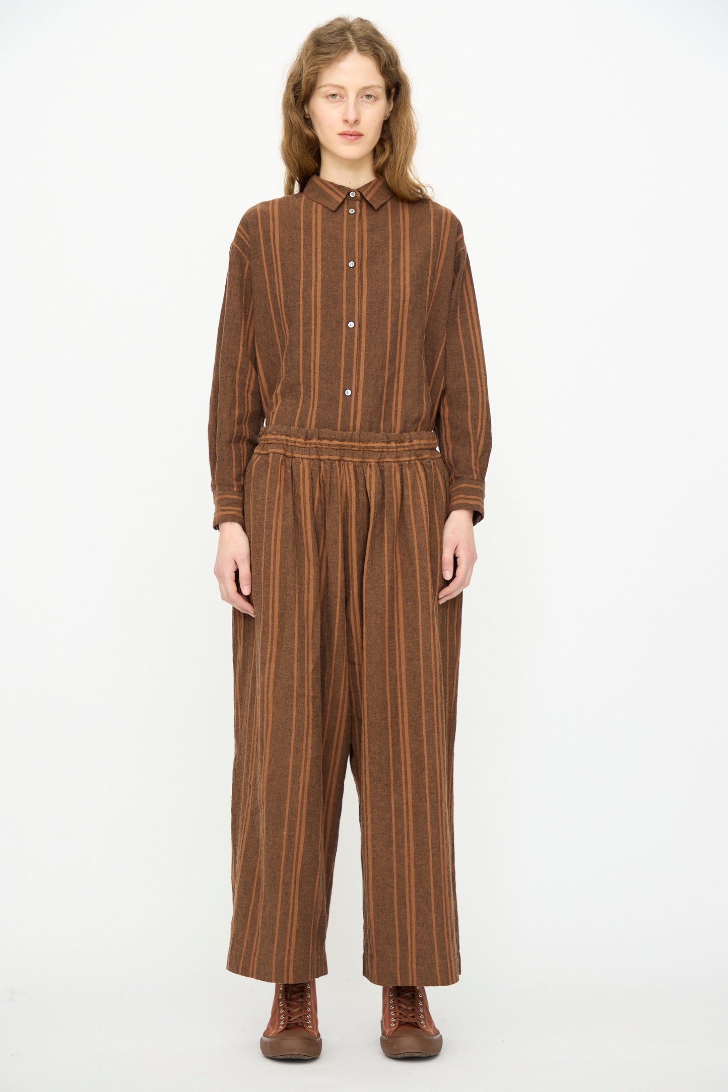 A person faces forward against a white background, wearing Ichi Antiquités' Linen Cotton Random Stripe Pant in Brown with an elastic waist, paired with a brown long-sleeve shirt and brown lace-up shoes.