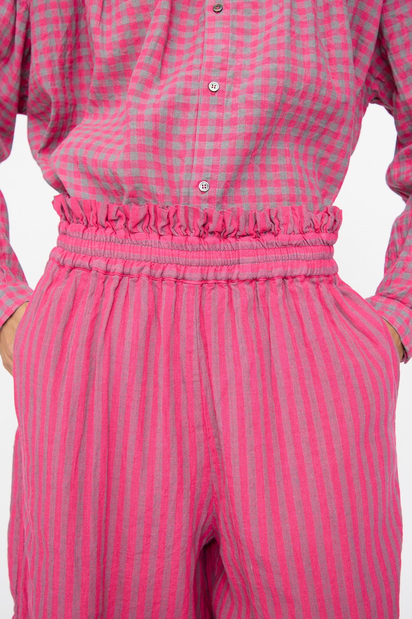 Someone wears a pink and green checkered button-up shirt tucked into Ichi Antiquités’ Linen Cotton Stripe Pants in Pink, featuring a cropped wide-leg fit, elastic waist, and ruffled accents.
