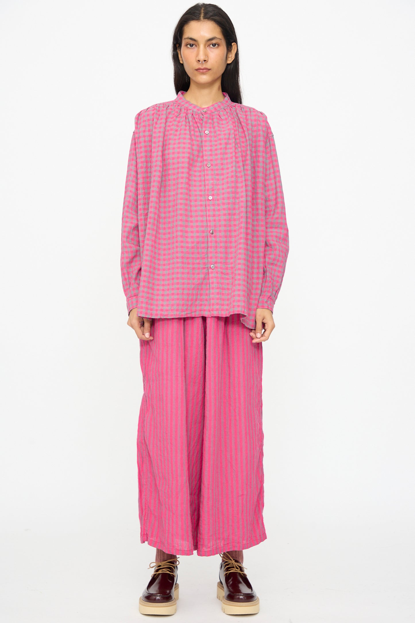 A person wears Ichi Antiquités' Linen Cotton Stripe Pants in Pink, which are cropped with a wide leg and elasticated waist, paired with a loose long-sleeve shirt and platform shoes, against a plain white background.