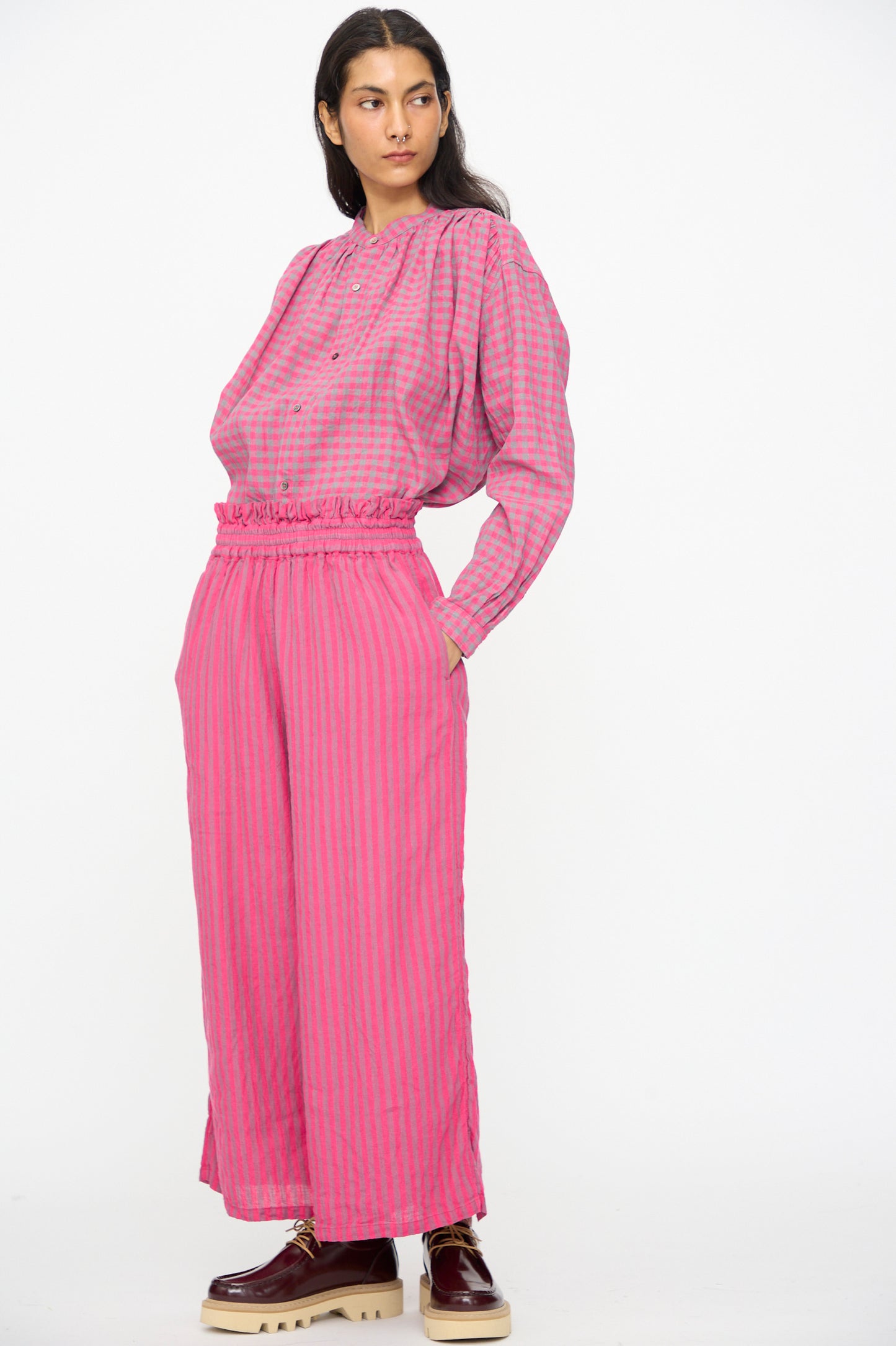A person wearing Ichi Antiquités Linen Cotton Stripe Pants in Pink styled with a loose, long-sleeve checkered top and platform shoes, standing against a plain white background.