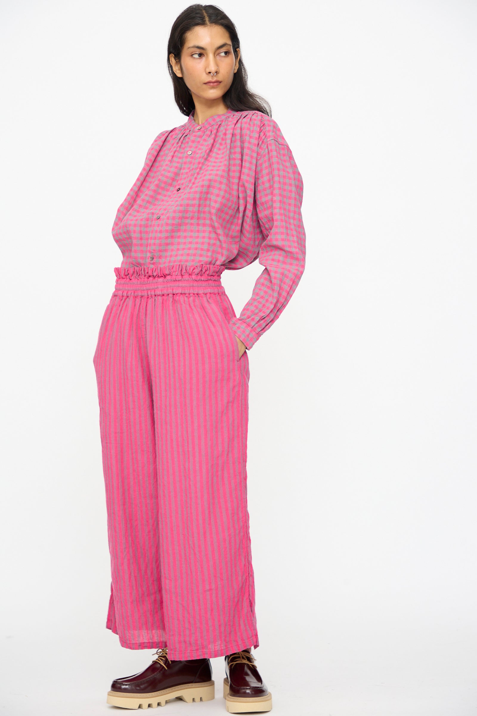 A person wearing Ichi Antiquités Linen Cotton Stripe Pants in Pink styled with a loose, long-sleeve checkered top and platform shoes, standing against a plain white background.