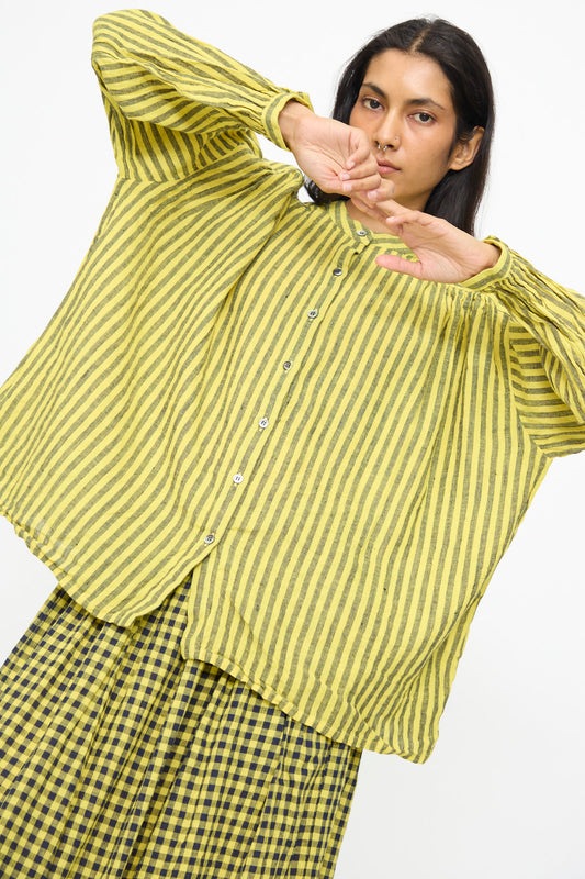 Someone poses with arms raised in front of a white background, wearing the Ichi Antiquités Linen Cotton Stripe Shirt in Yellow paired with a matching checkered skirt.