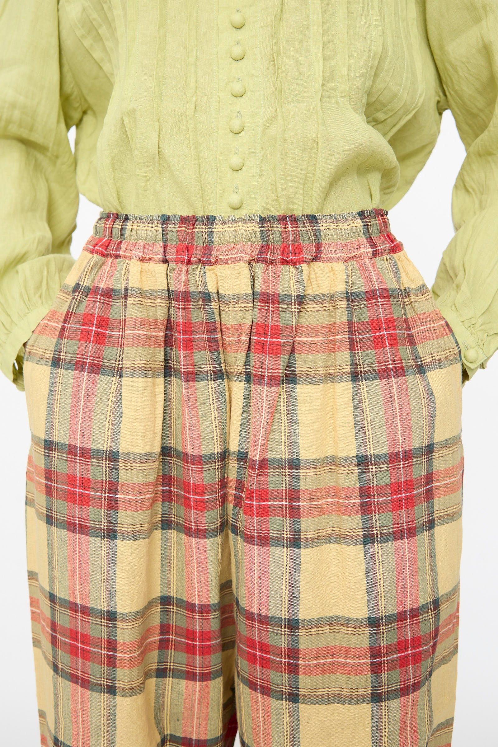 Person wearing a light green buttoned blouse with long sleeves and Ichi Antiquités Linen Cotton Tartan Pants in Butter Yellow, hands in pockets.