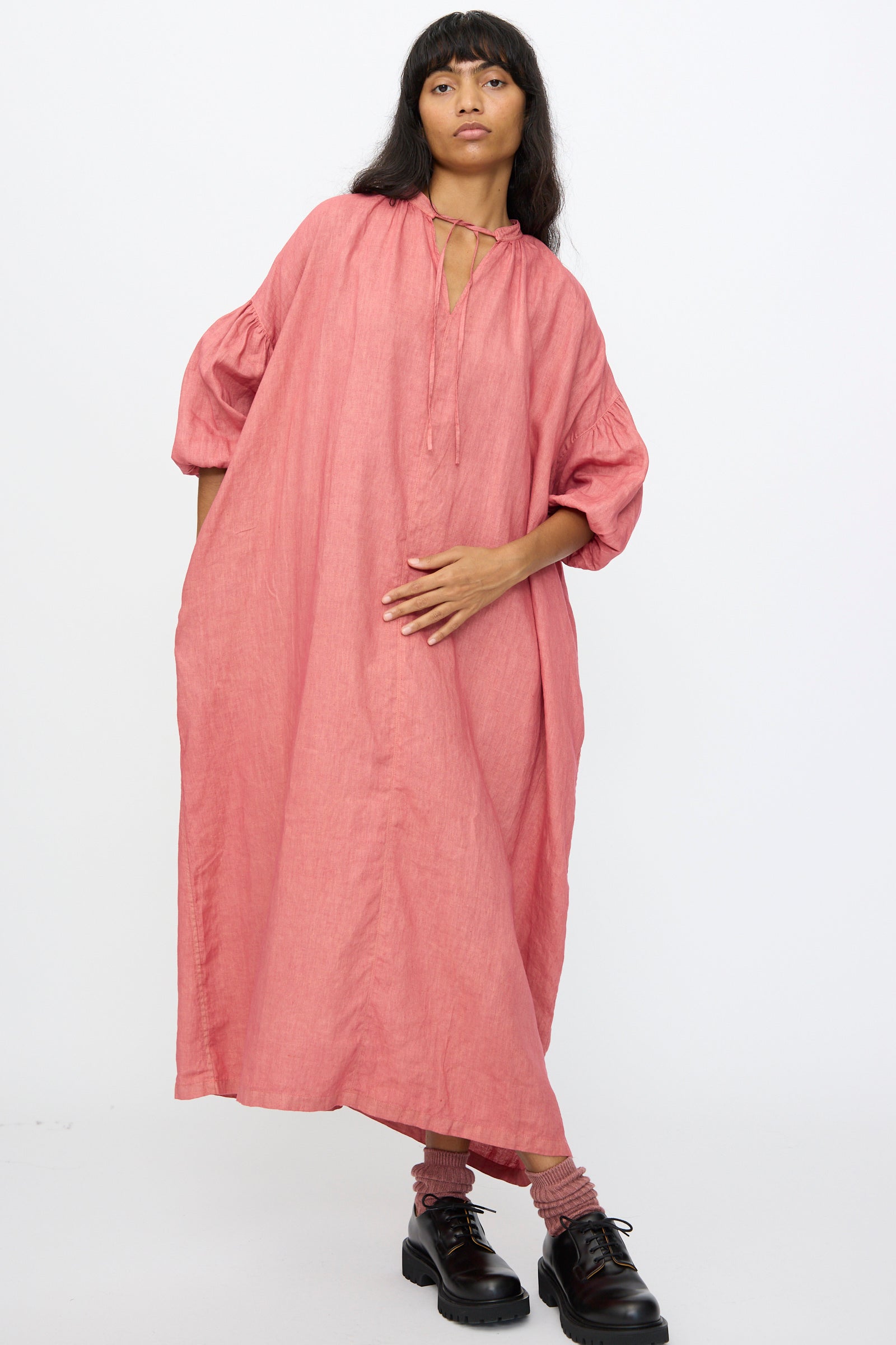 A person wearing the Ichi Antiquités Linen Dress in Pink, styled with black shoes and socks, stands against a plain white background.