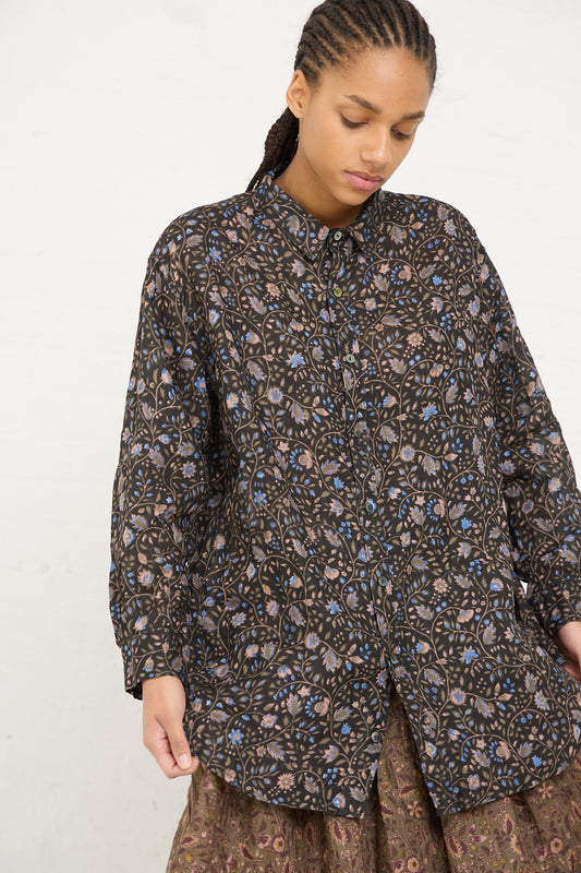 A person wearing a Linen Floral Shirt in Black by Ichi Antiquités with hands slightly tucked into pockets stands against a plain background.