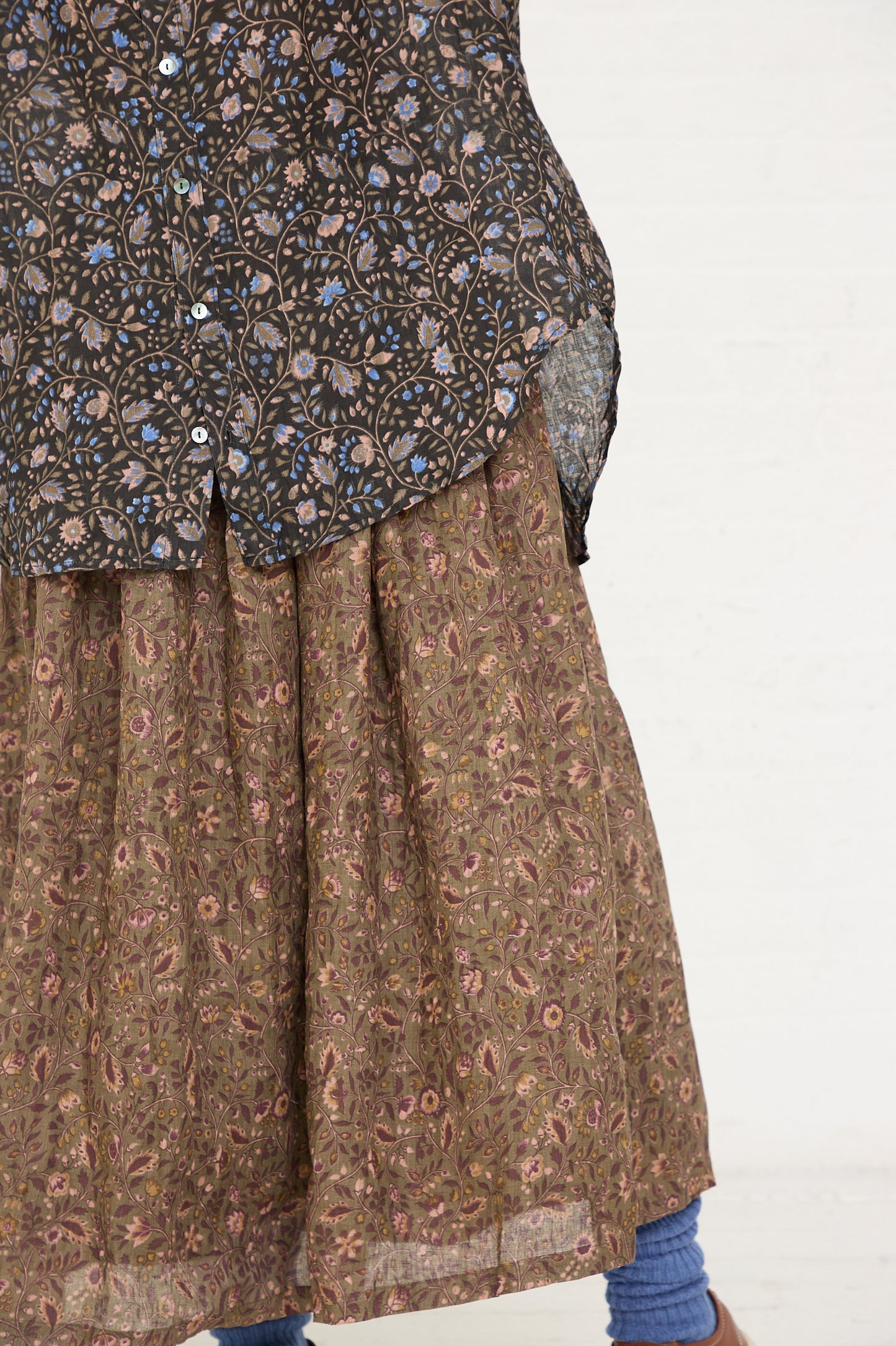 Partial view of a person wearing a Linen Floral Shirt in Black by Ichi Antiquités and a patterned skirt with a glimpse of blue socks.