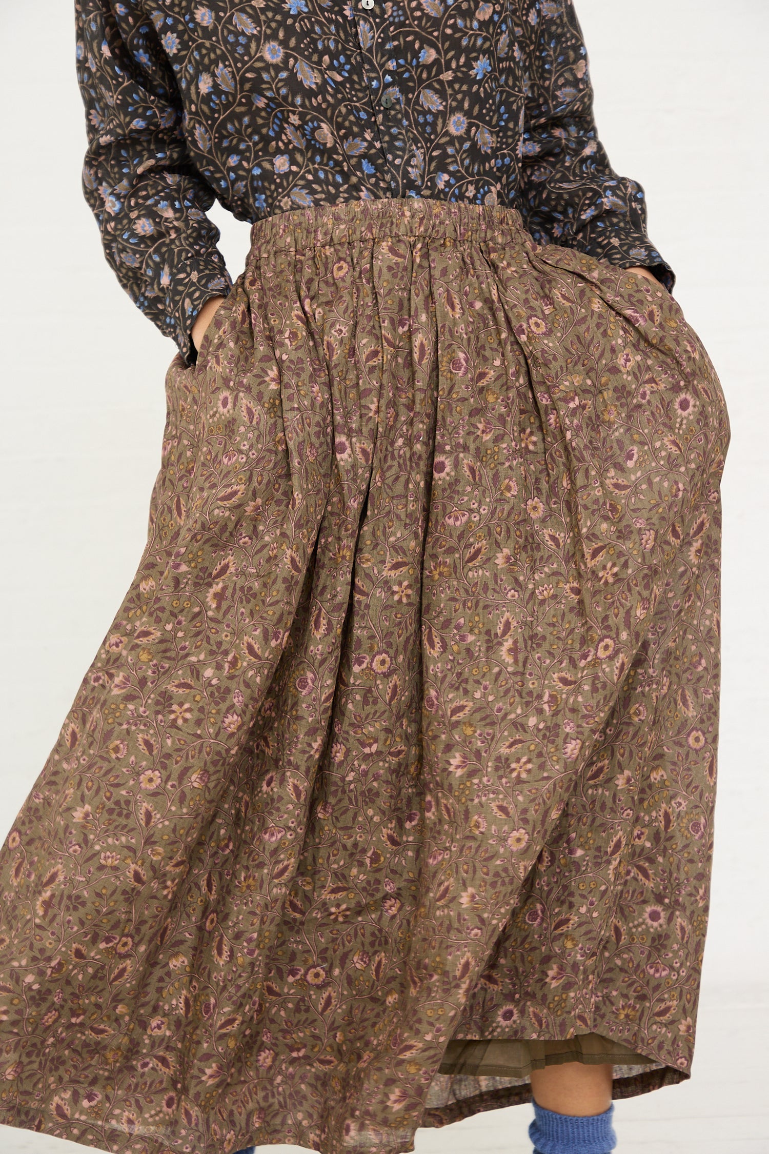 A person wearing a patterned blouse and a long, Linen Floral Skirt in Mocha from Ichi Antiquités with hands placed on the hips.